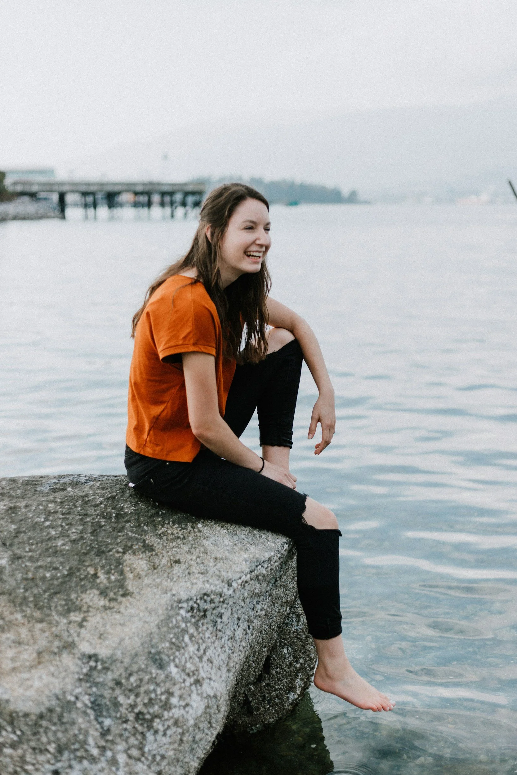 woman sitting on rock by waterside smiling