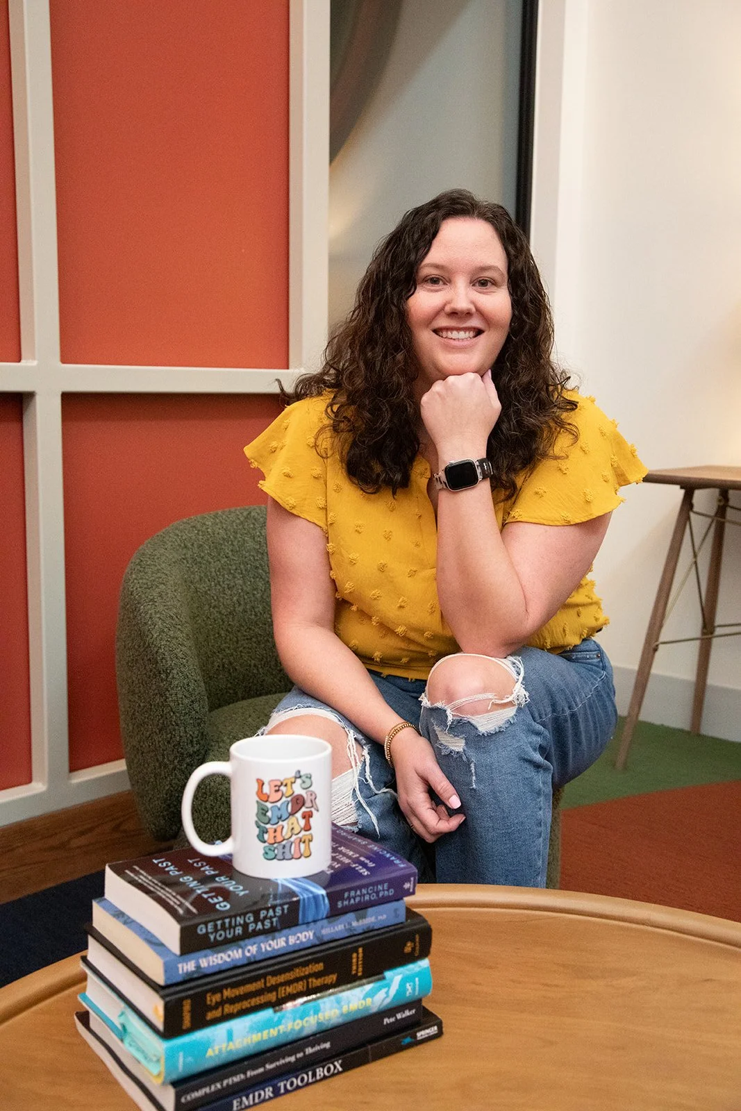 Dallas EMDR therapist sitting smiling with trauma books in front of her
