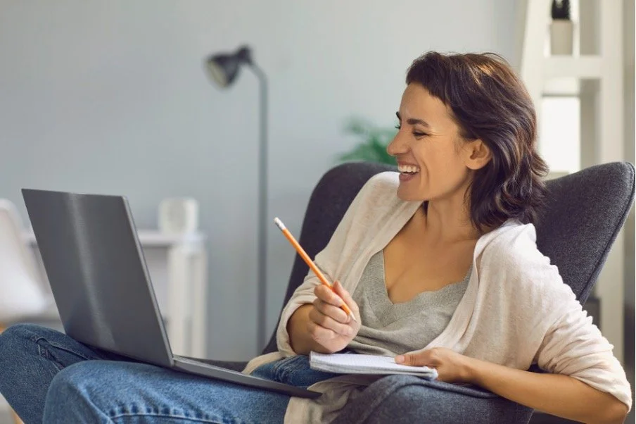 woman smiling at laptop with pencil and journal in her hand in EMDR therapy