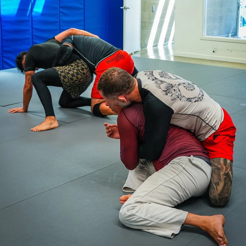 Two pairs of people practicing Brazilian Jiu-Jitsu on a mat in a training gym, engaging in grappling techniques.