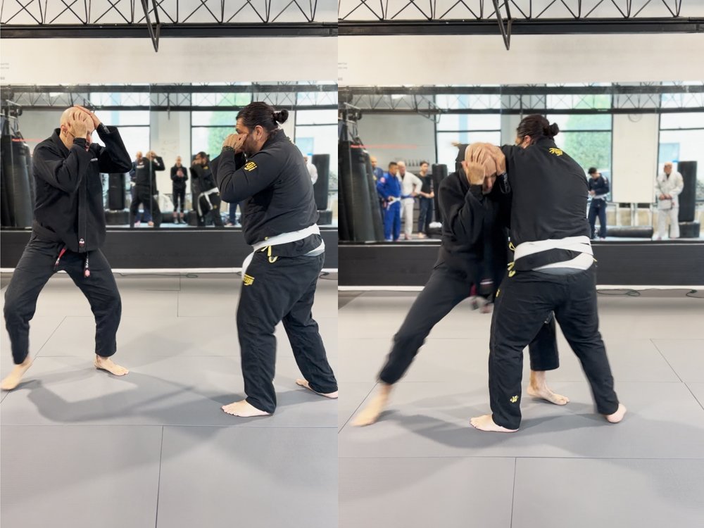 Two martial artists practice Brazilian Jiu-Jitsu techniques in a gym with a mirror, with onlookers and other martial artists in the background.