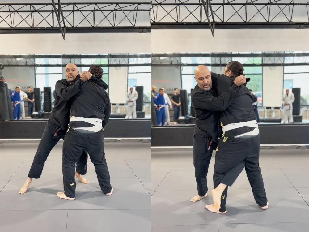 Two men practicing Brazilian Jiu-Jitsu on a mat, wearing black gi uniforms, with one demonstrating a chokehold technique in a martial arts gym.