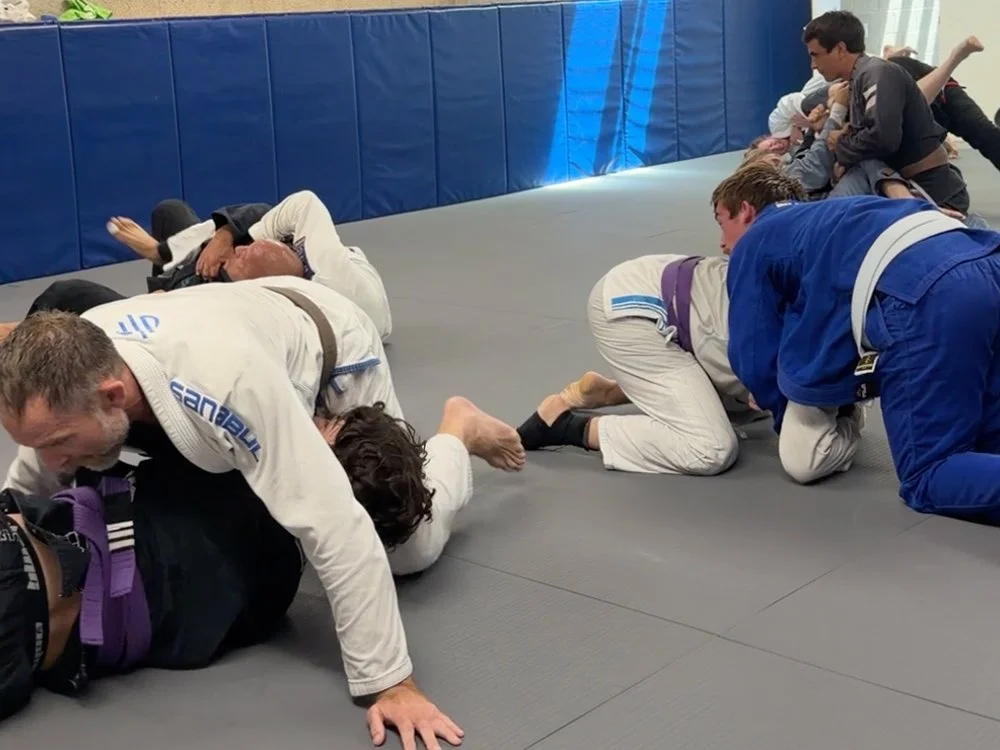 Jiu Jitsu practitioners in a training class practicing ground grappling techniques on a padded mat, involved in close contact positions.