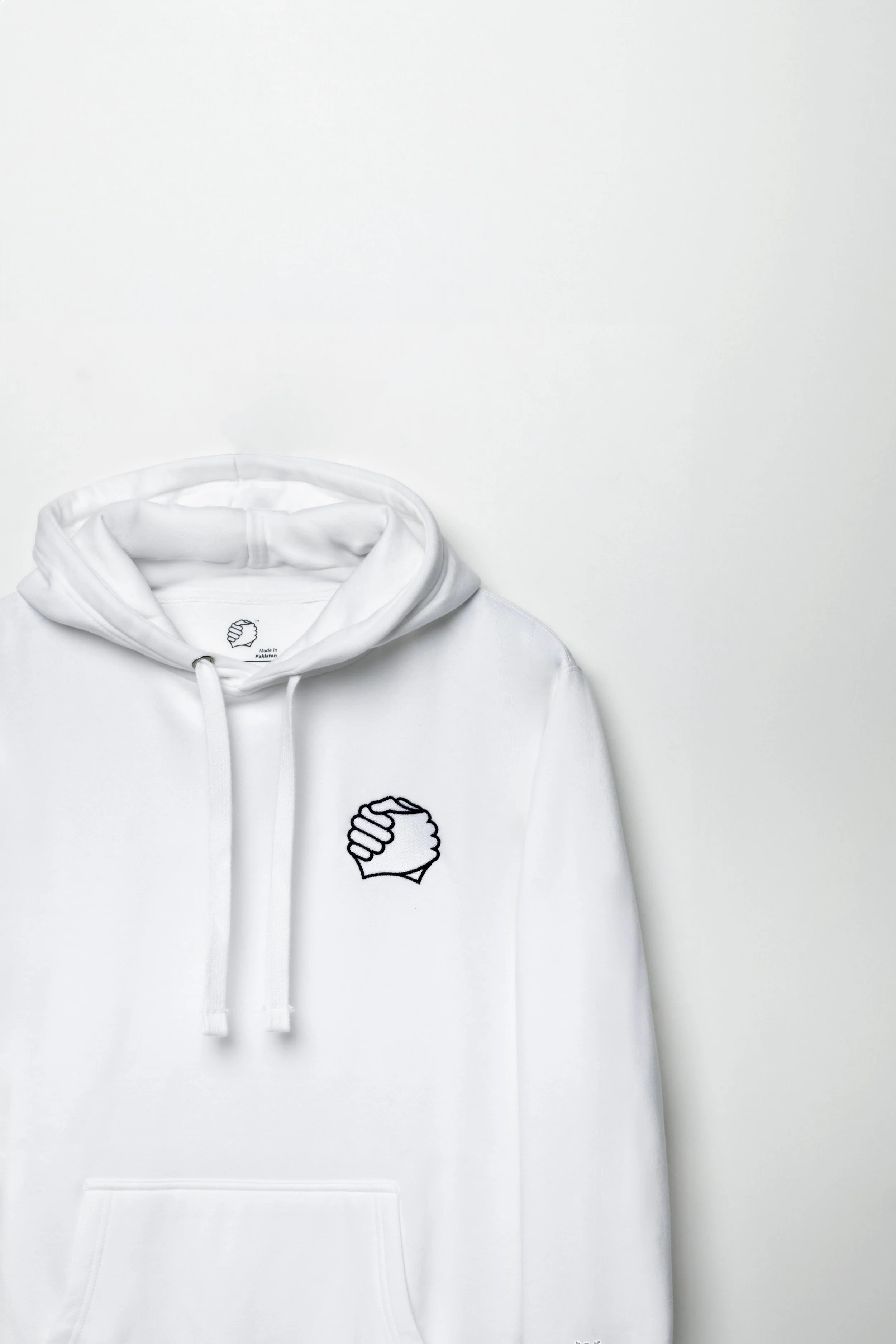 Close-up of clasped-hands embroidery on the chest of the ADVIKATE Classic Hoodie Series I in White, showing stitch detail and texture.