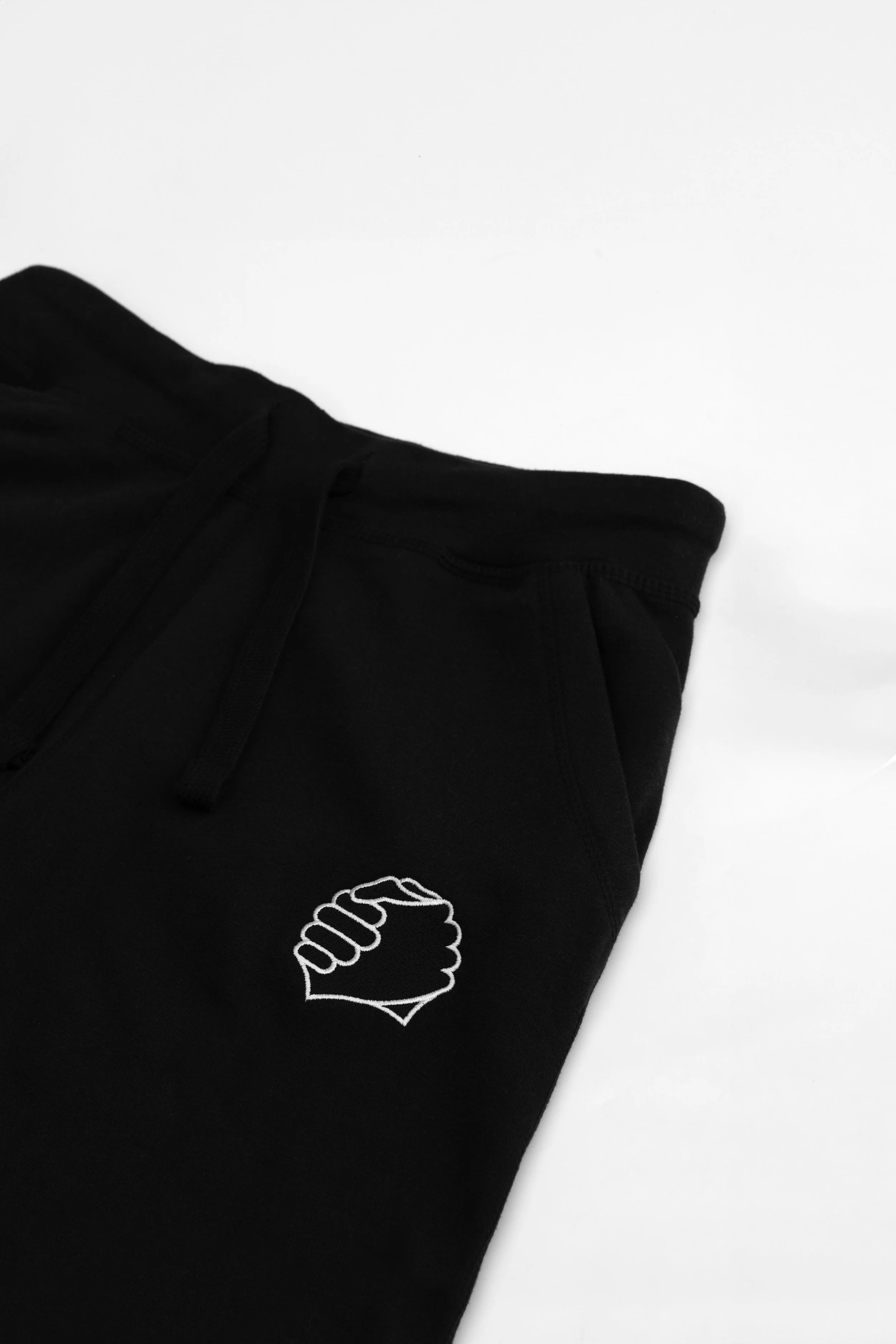 Close-up of clasped-hands embroidery on the left thigh of the ADVIKATE Classic Trackpants Series I in Black, showing stitch detail and texture.