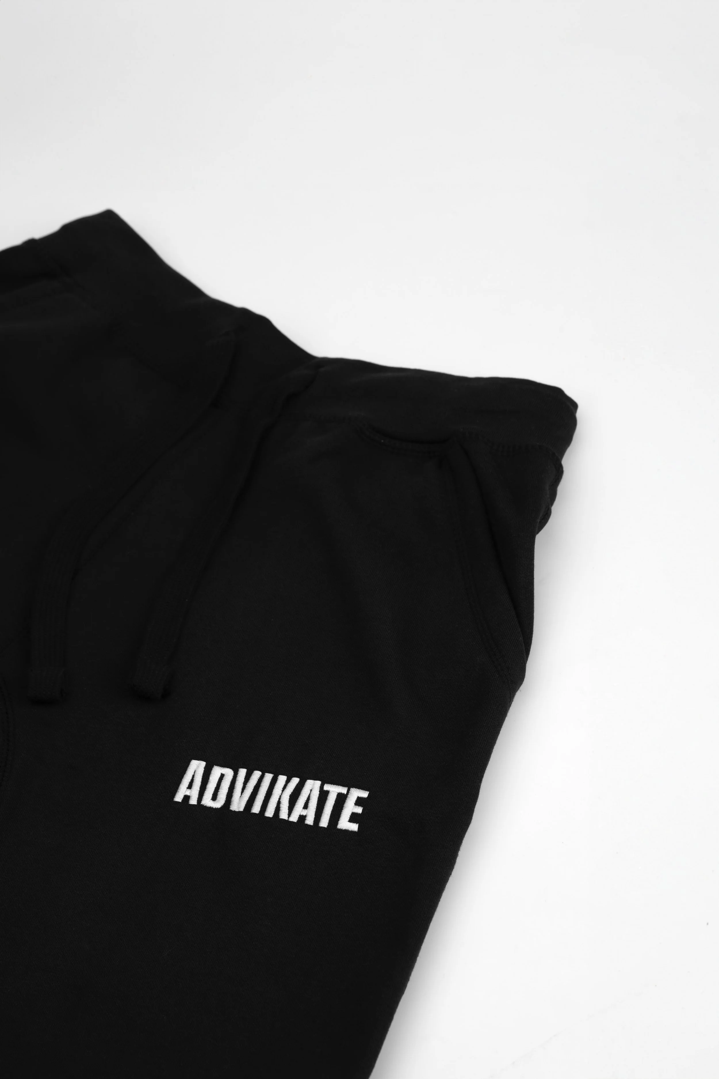 Close-up of ADVIKATE text embroidery on the left thigh of the ADVIKATE Classic Trackpants Series II in Black, showing stitch detail and texture.