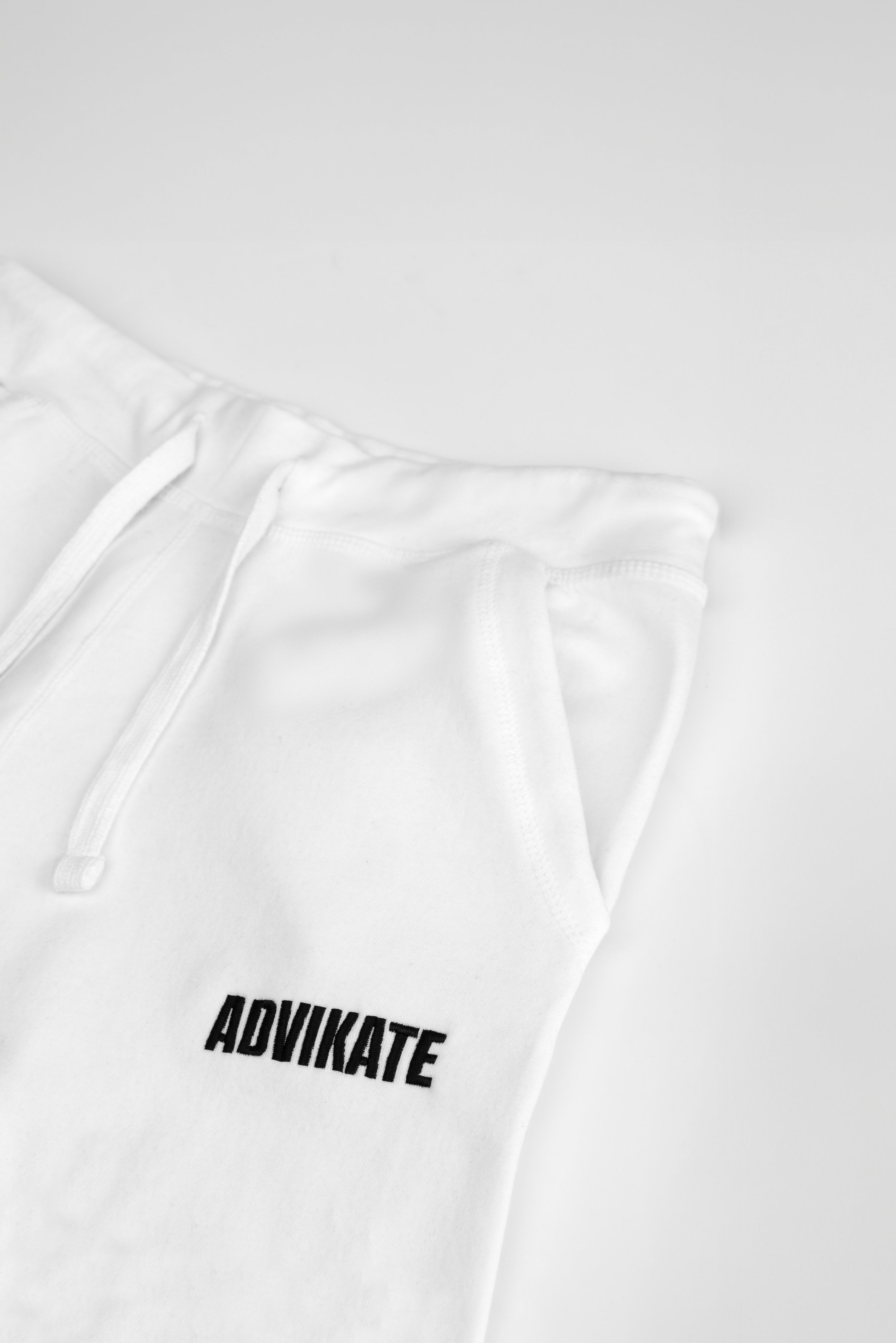 Close-up of ADVIKATE text embroidery on the left thigh of the ADVIKATE Classic Trackpants Series II in White, showing stitch detail and texture.