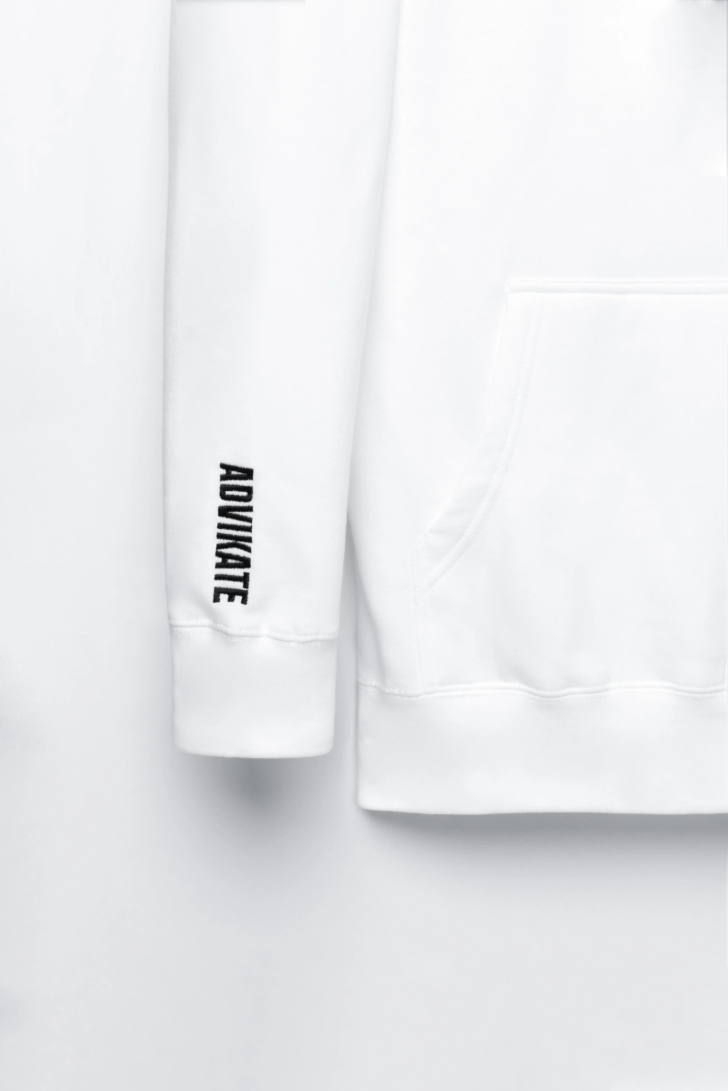 Close-up of ADVIKATE text logo embroidery on the right sleeve of the ADVIKATE Classic Hoodie Series I in White.