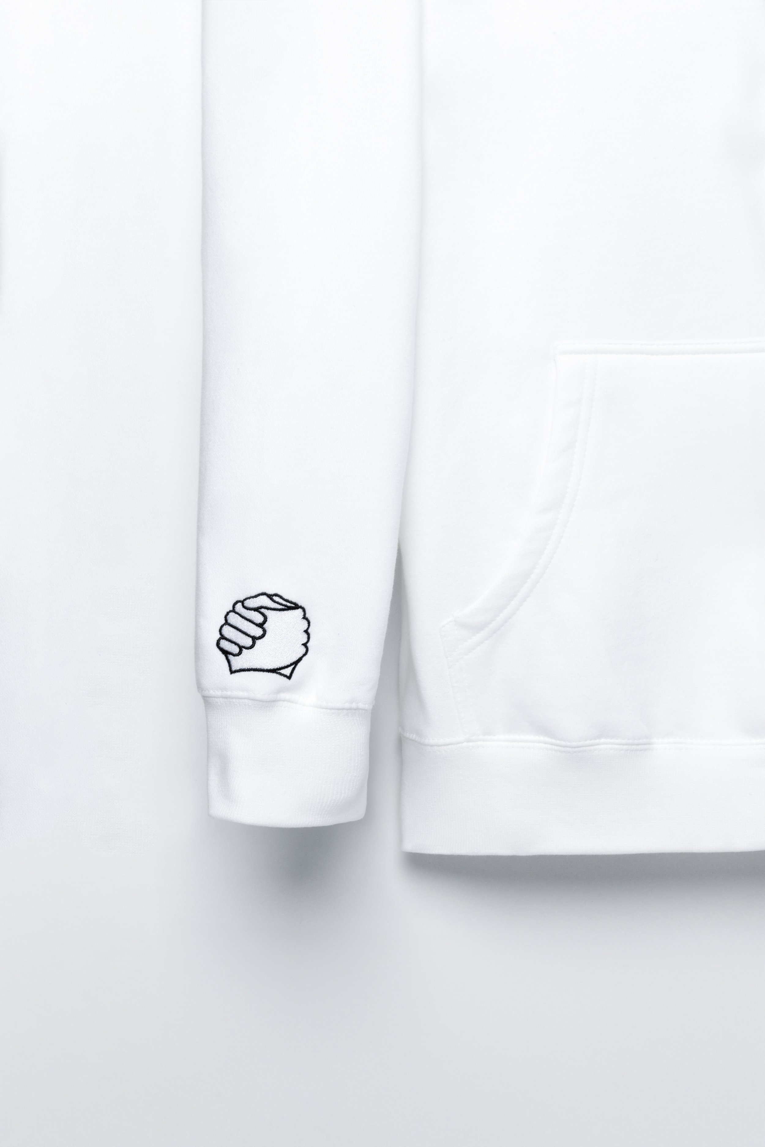 Close-up of clasped-hands embroidery on the right sleeve of the ADVIKATE Classic Hoodie Series II in White.
