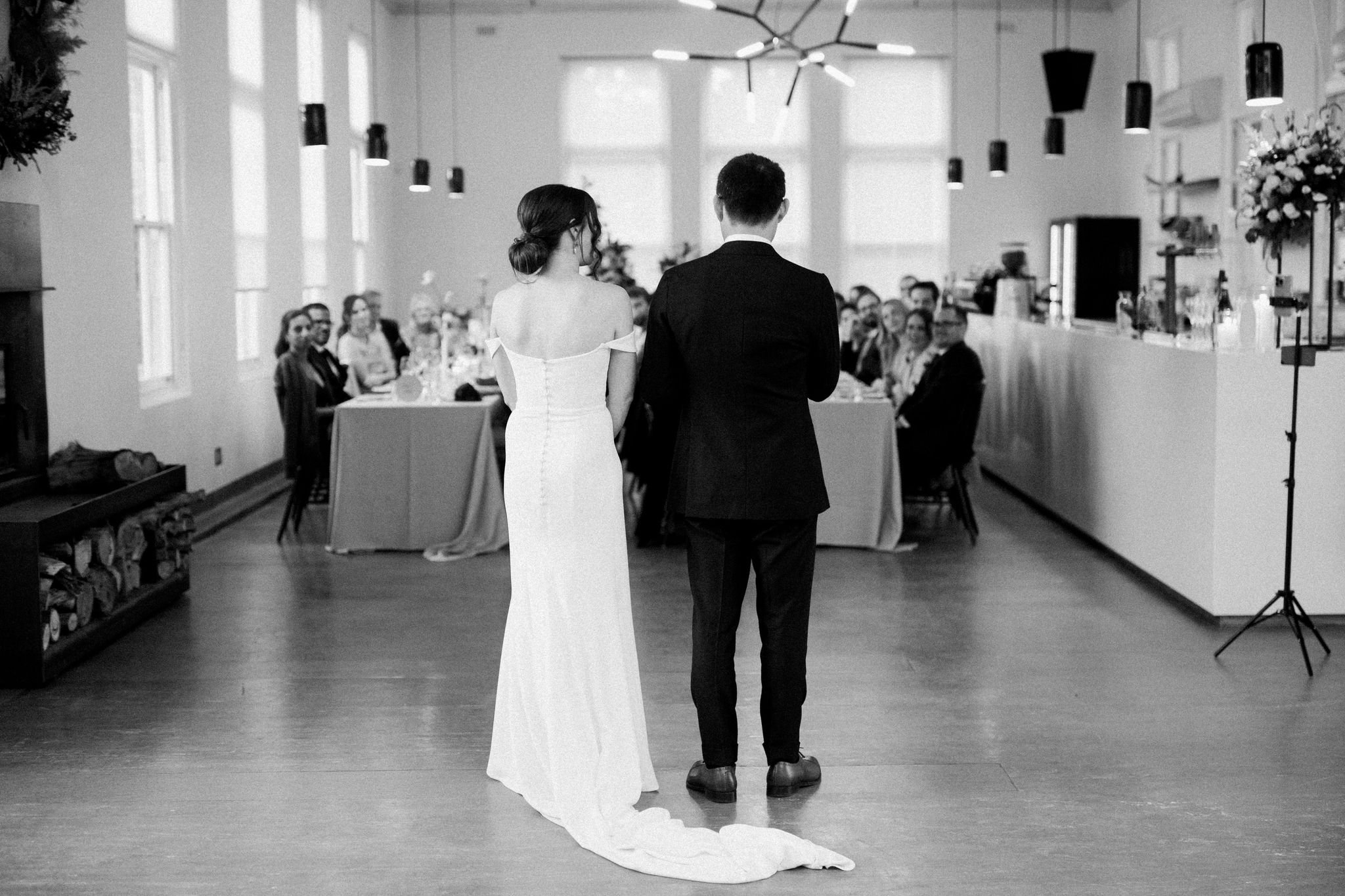 Bride and groom standing together during their wedding ceremony in an indoor venue, facing a seated audience.