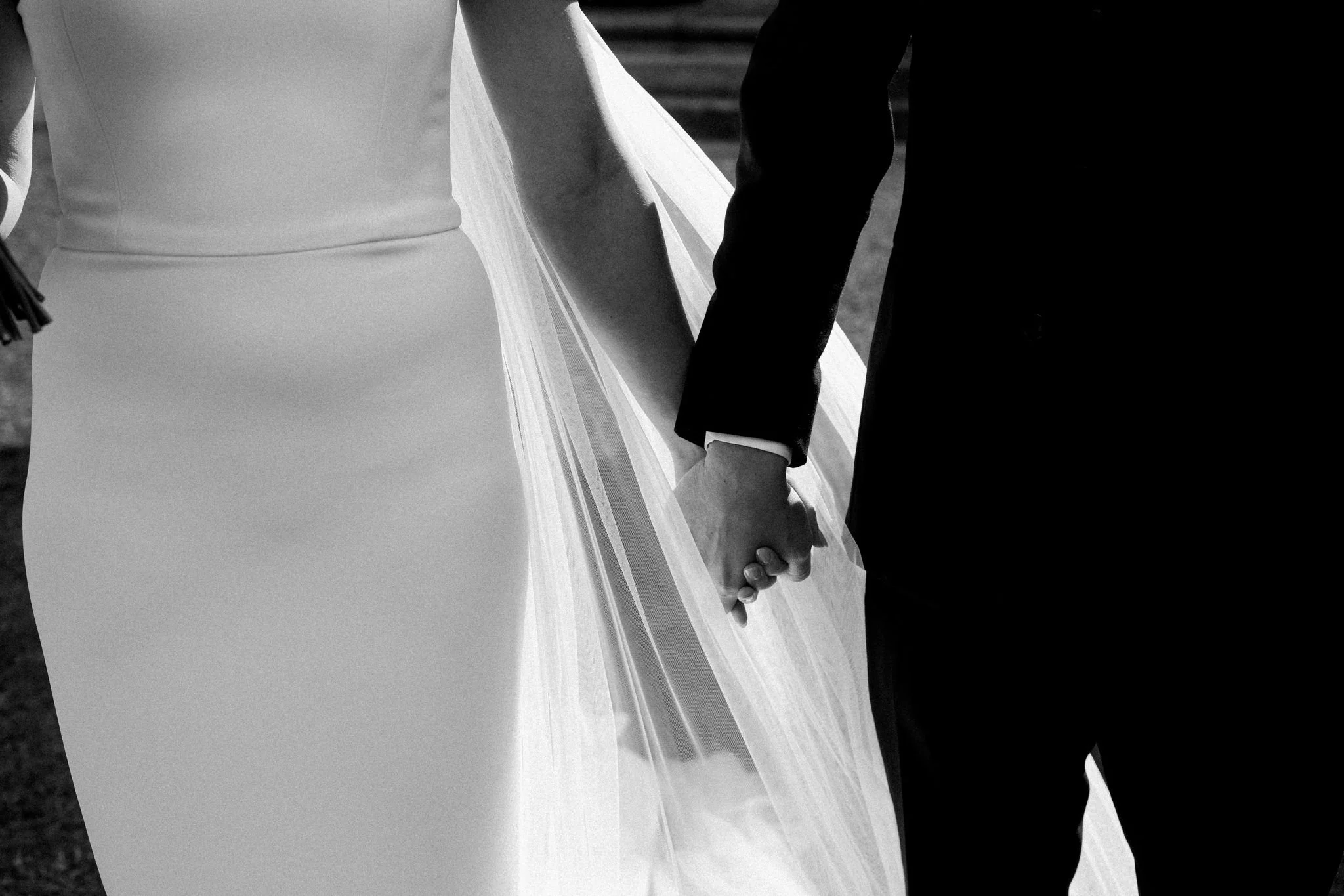 Close-up of a bride and groom holding hands during their wedding ceremony, with the bride in a white dress and the groom in a dark suit.