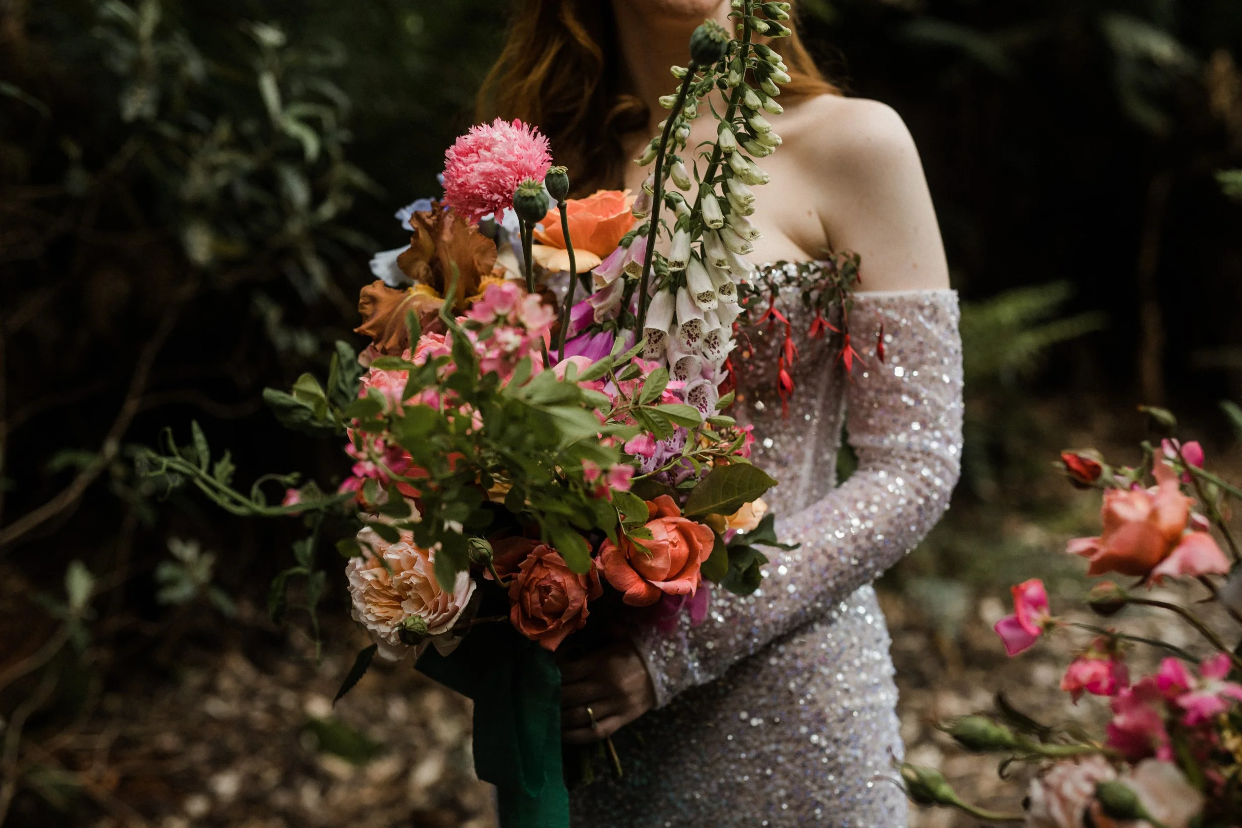 A woman in a sparkly off-shoulder dress holding a colorful bouquet of flowers outdoors.