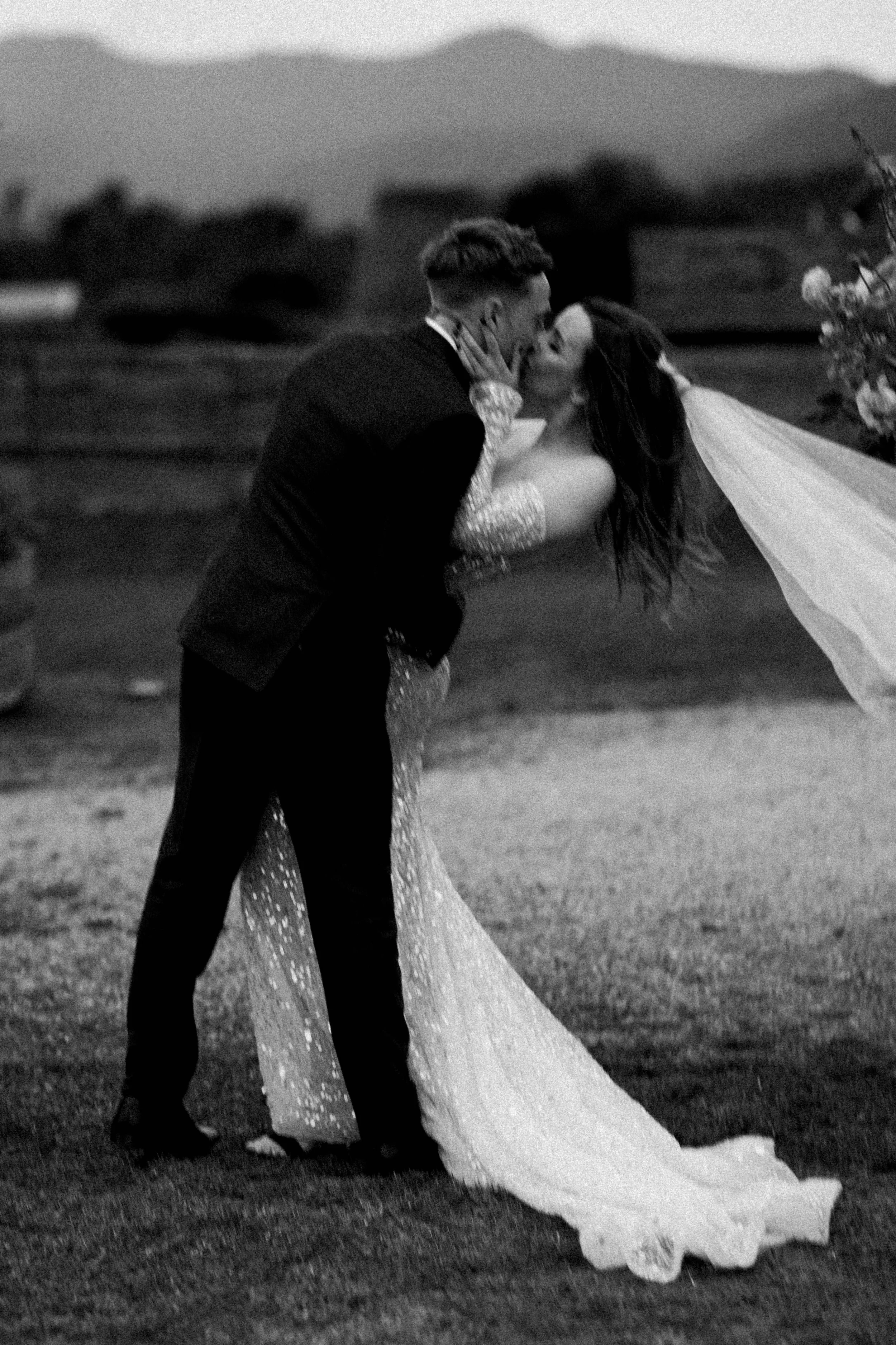 A couple sharing a romantic kiss at sunset, dressed in formal wedding attire, with the groom dipping the bride while they kiss outdoors.