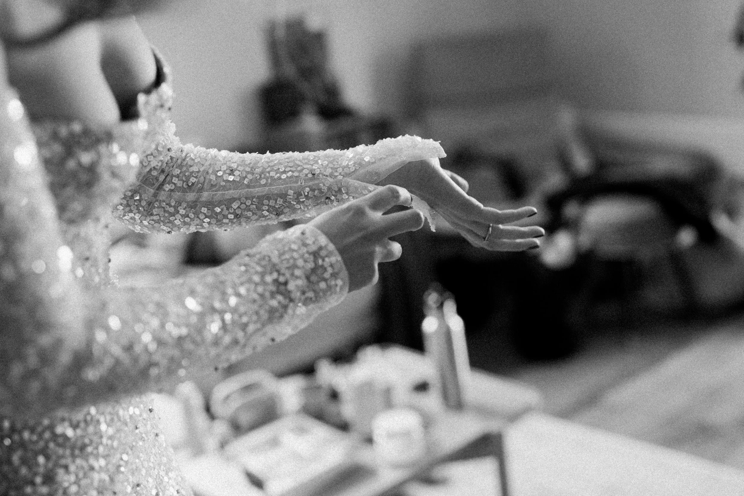 Close-up of a bride's hands with manicured nails and ring, wearing a sparkly dress, as she applies nail polish.