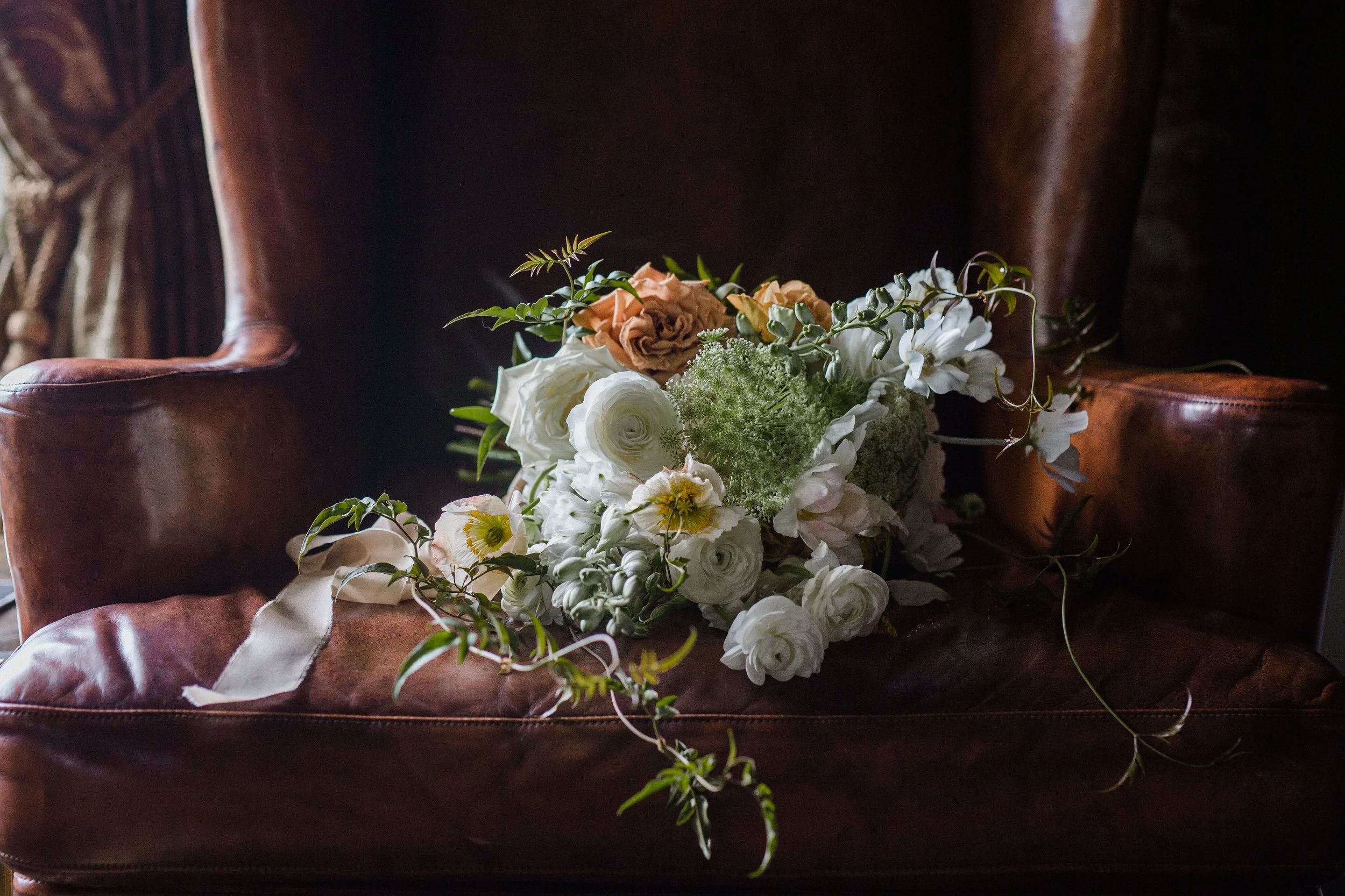 A bouquet of white and peach flowers resting on a brown leather armchair.