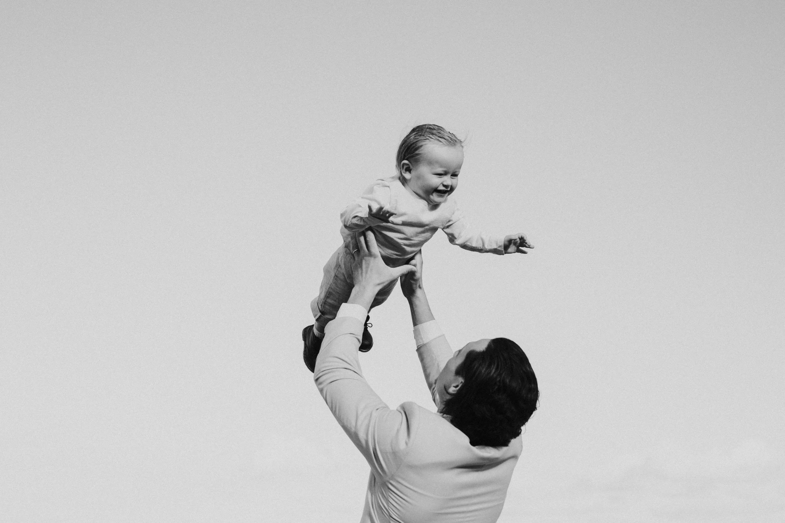 A person lifting a young child into the air with a clear sky in the background.