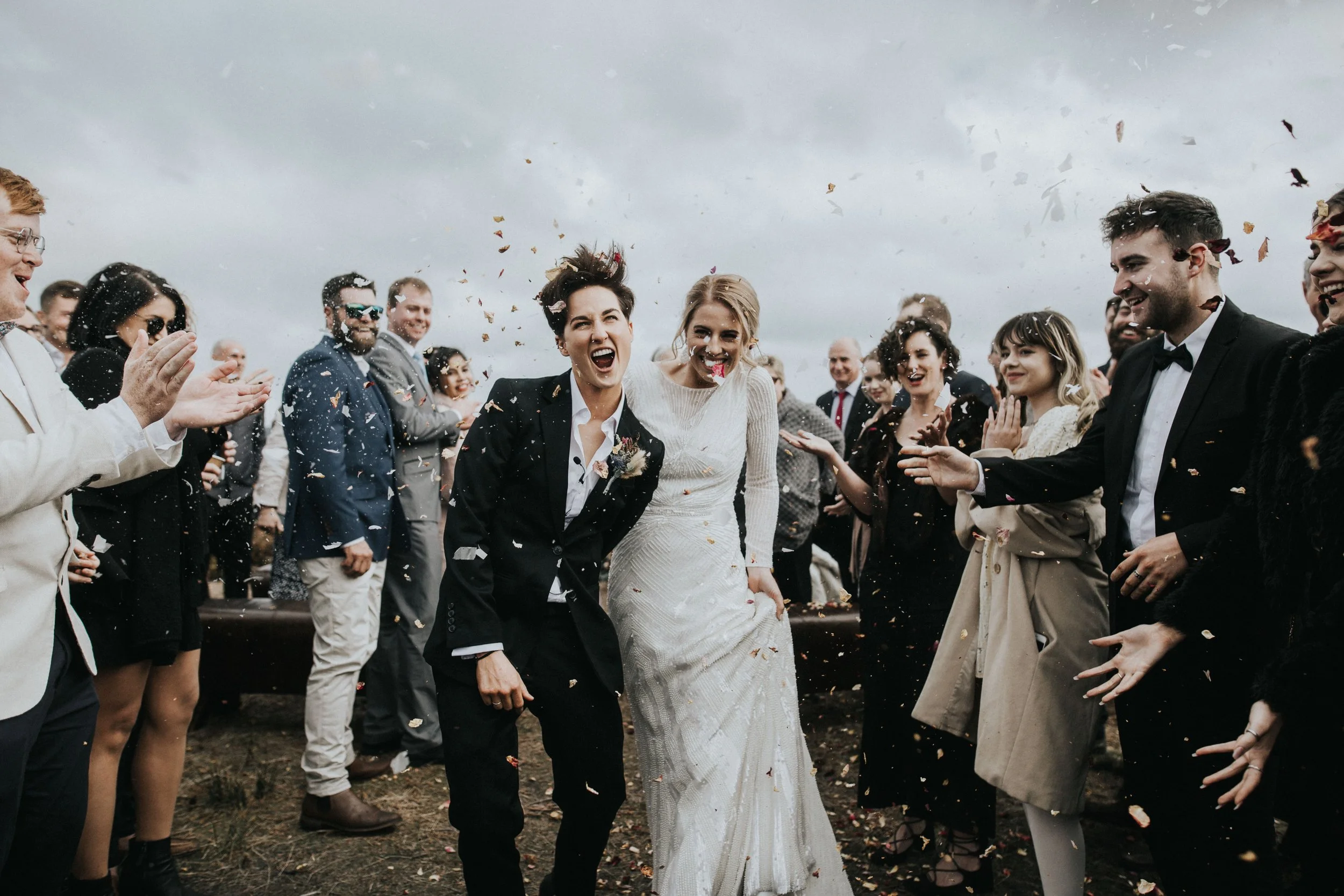 A wedding celebration outdoors with a wedding couple and guests throwing confetti.