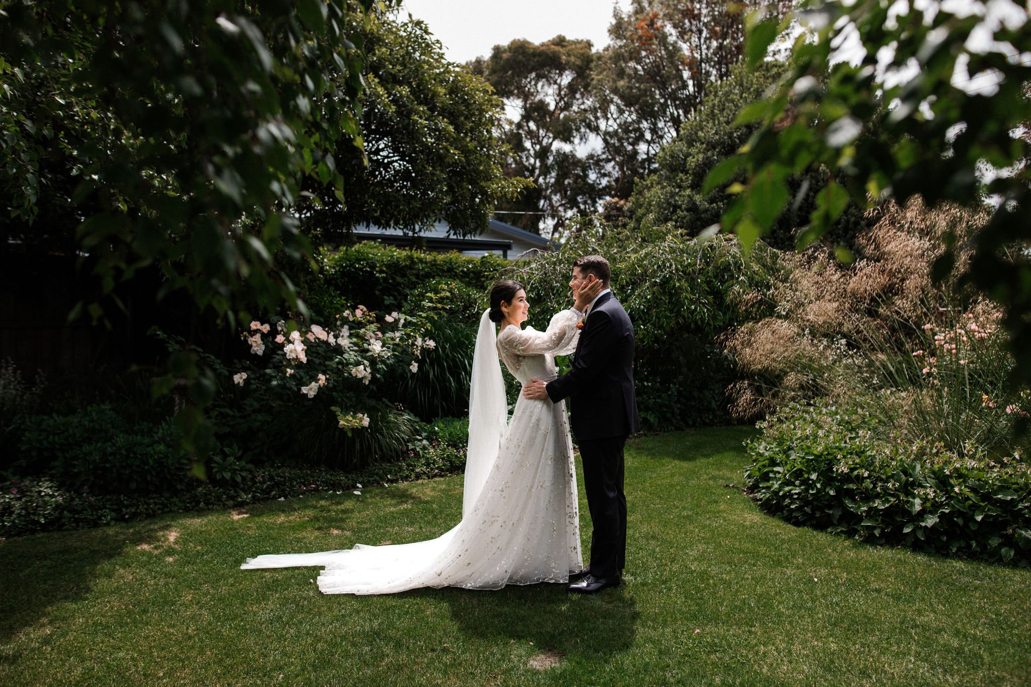 A bride and groom sharing a moment in a lush garden, surrounded by greenery, flowers, and trees during their wedding.
