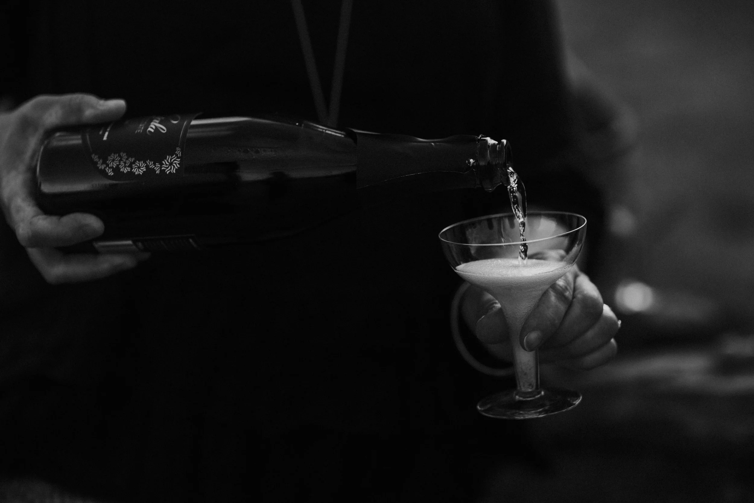 A person pours a drink from a bottle into a cocktail glass.
