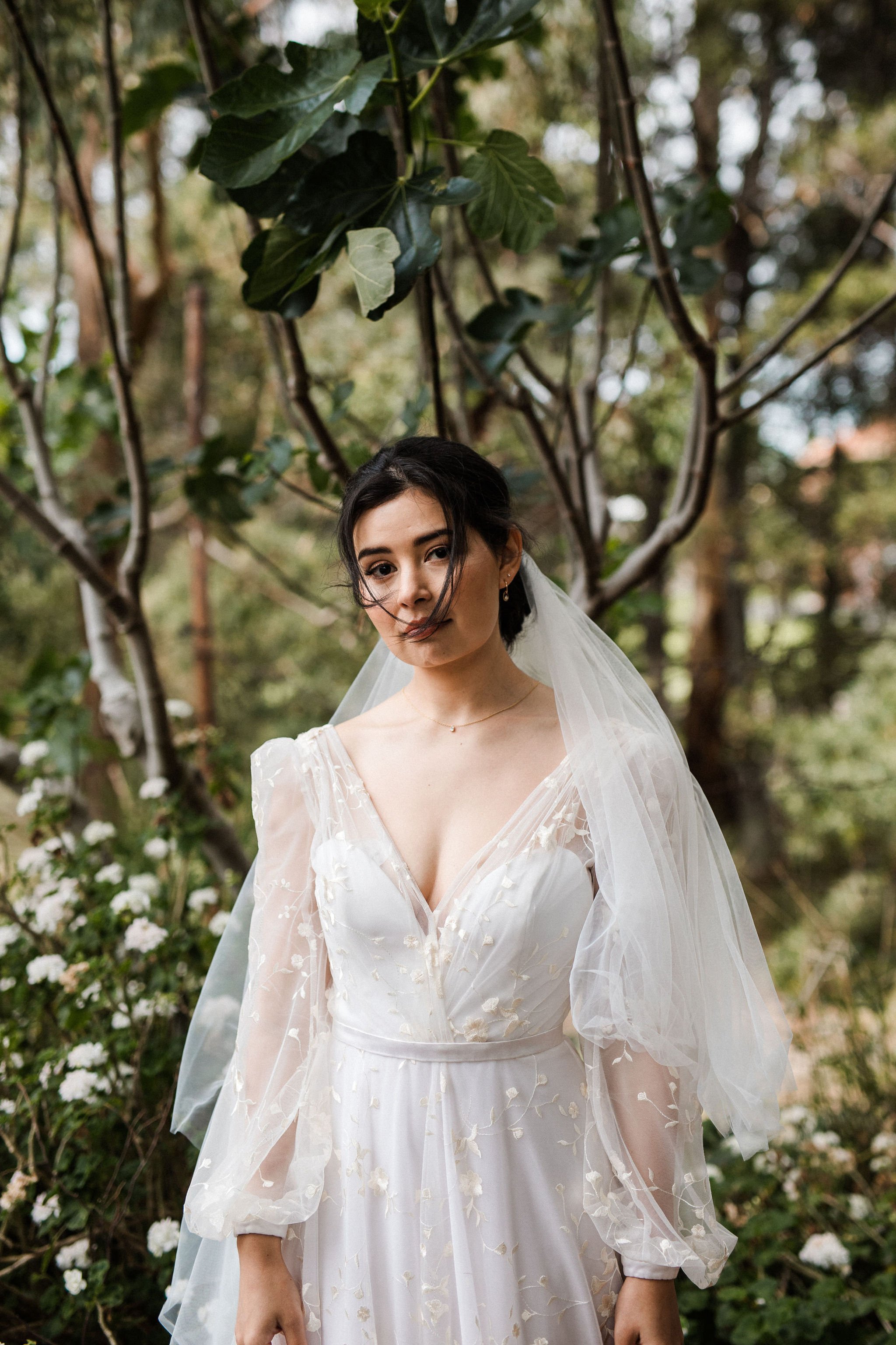 A woman in a wedding dress standing outdoors in a forested area.