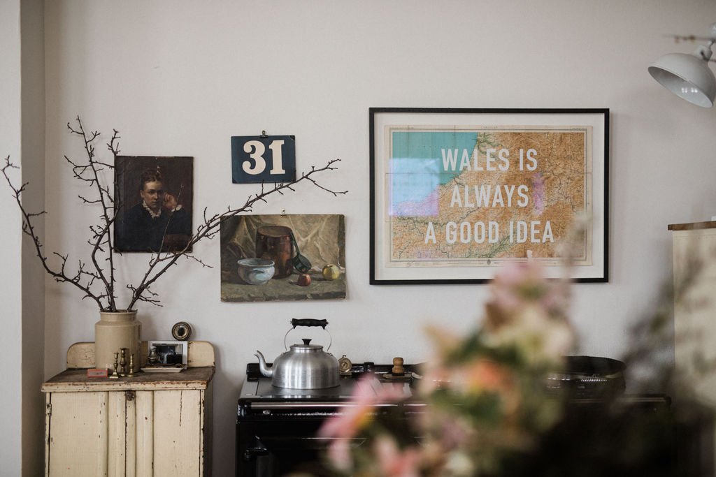Interior of a room with a kitchen stove, framed picture, wall art, vintage cabinet, and decorative branch arrangement.