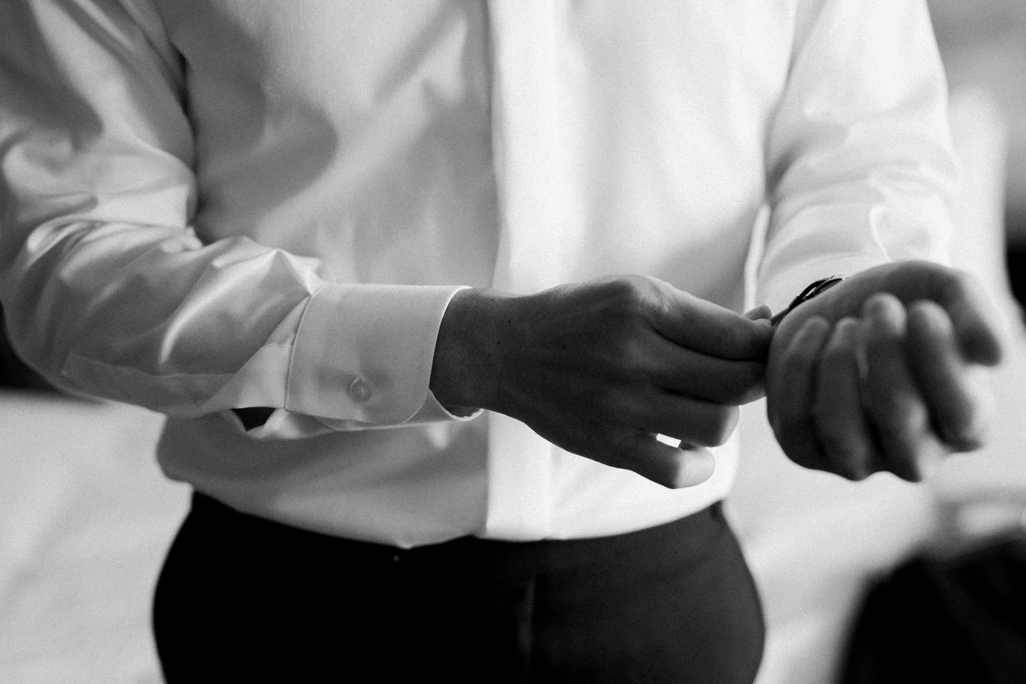 A person wearing a white dress shirt is adjusting a watch on their wrist.