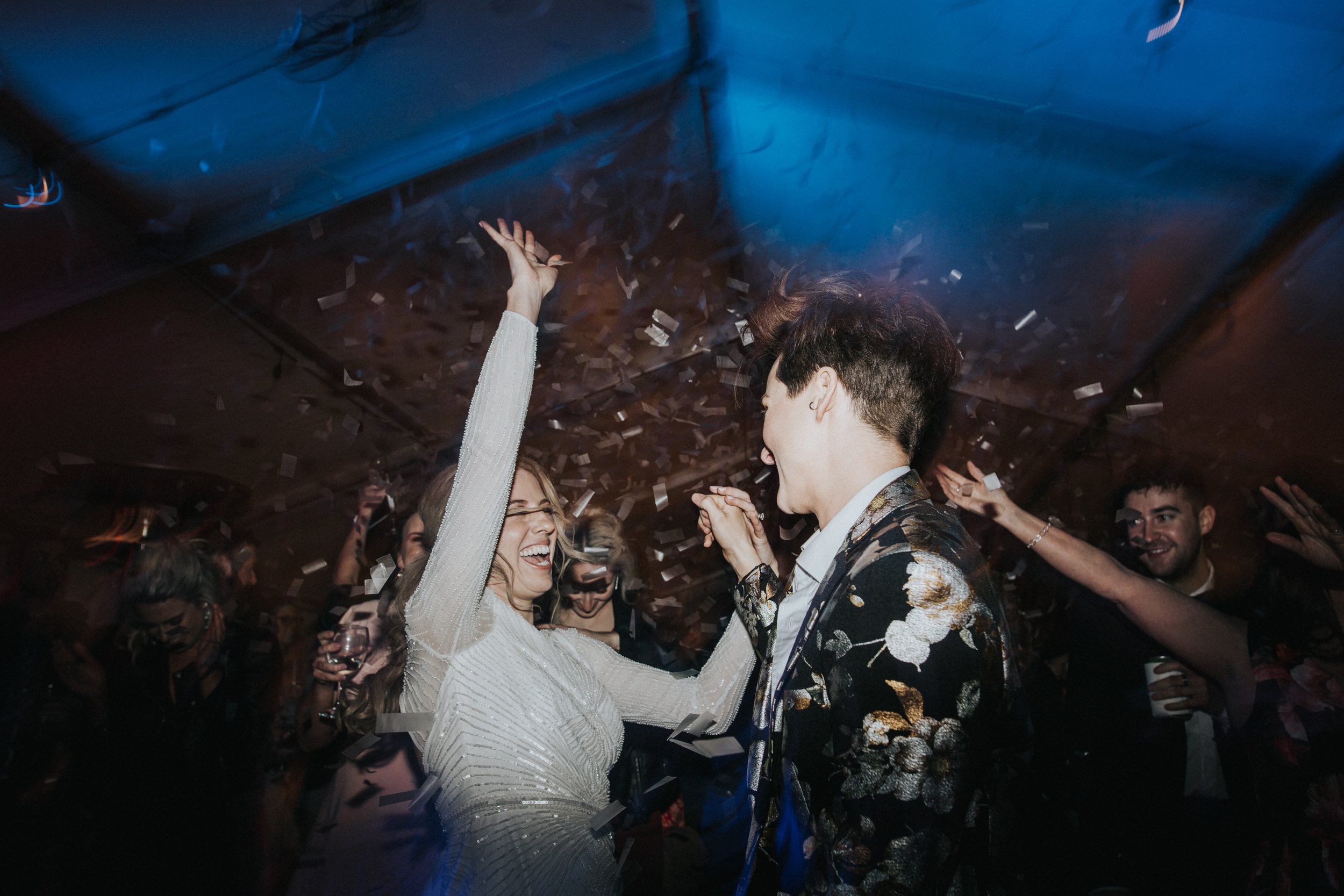 A couple dancing and celebrating at a party or wedding reception, surrounded by confetti and other guests.