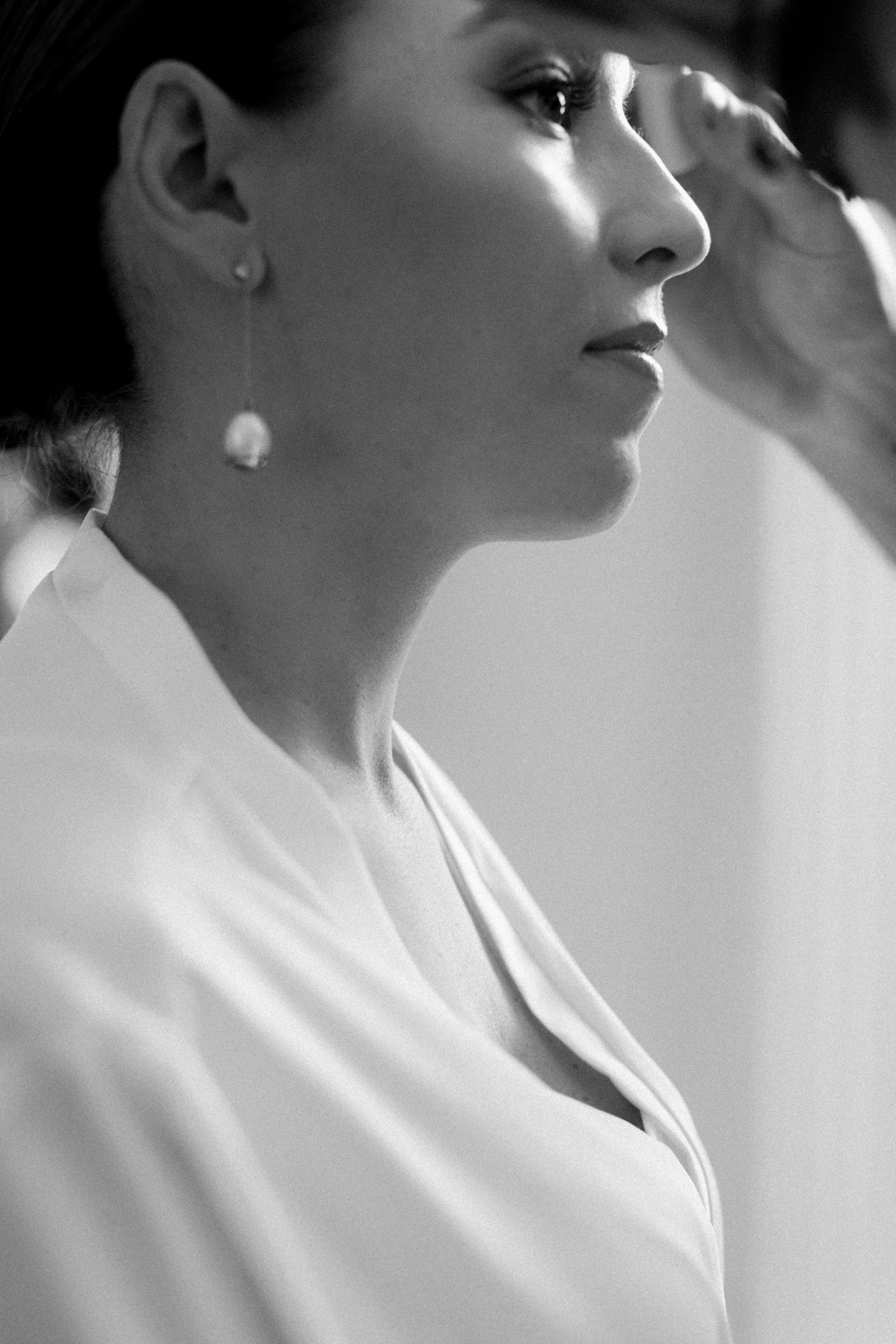 Black and white close-up side profile of a woman with an earring, wearing a white shirt.
