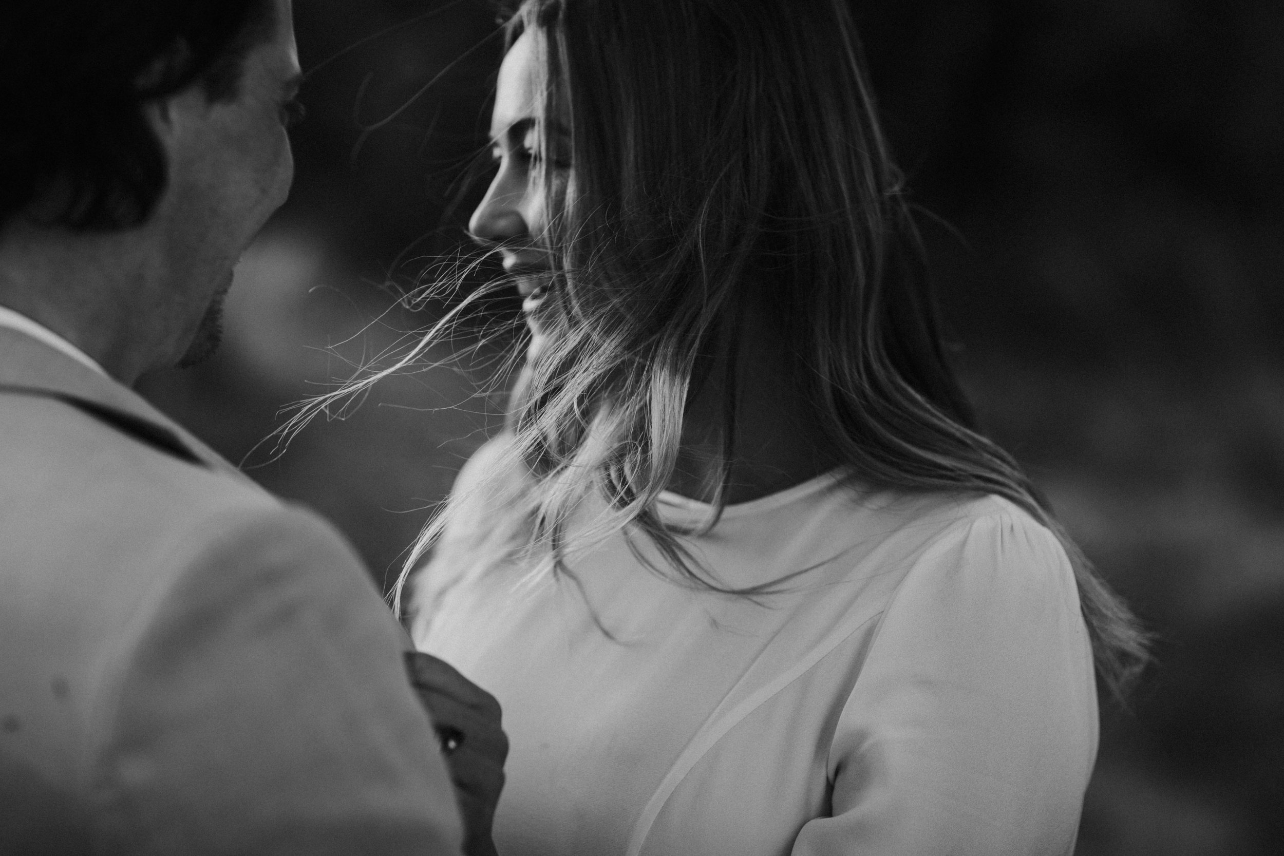 A black-and-white photo of a man and woman close together, smiling and looking at each other, outdoors.