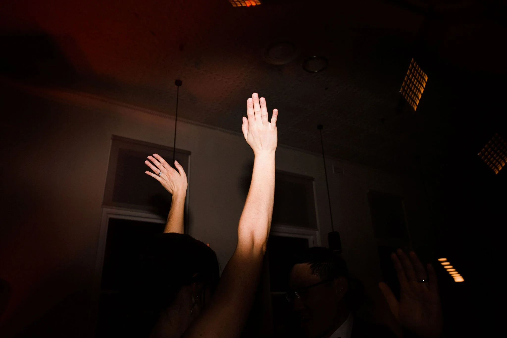 People raising their hands during a celebration or event in a dimly lit room.