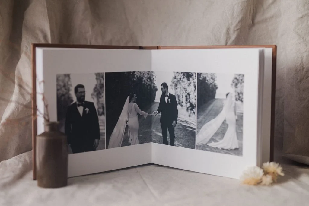 Open wedding photo album displaying three black-and-white images of a bride and groom outdoors.
