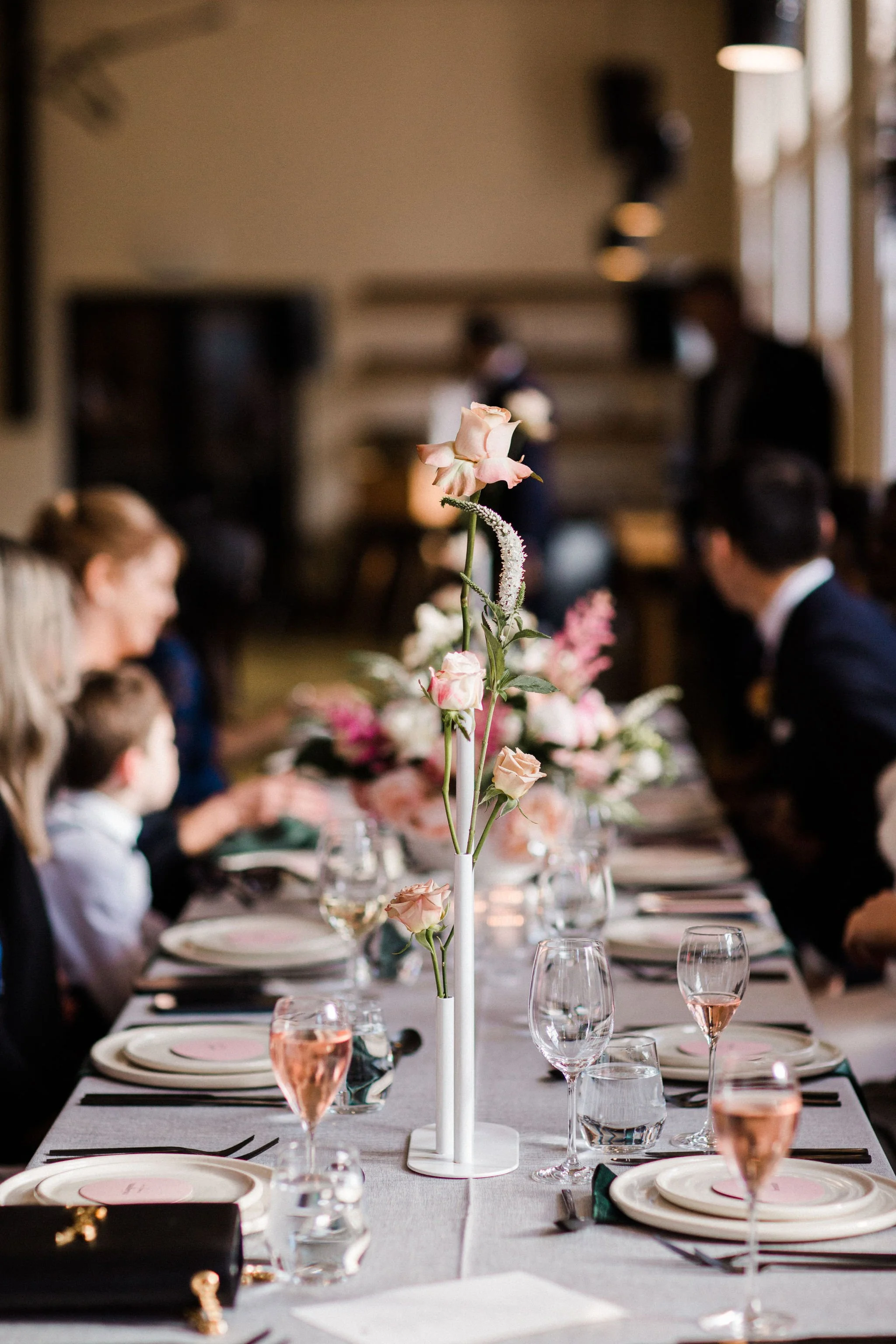 Elegant dining table with floral centerpiece, glassware, and place settings, at a formal event or wedding reception.