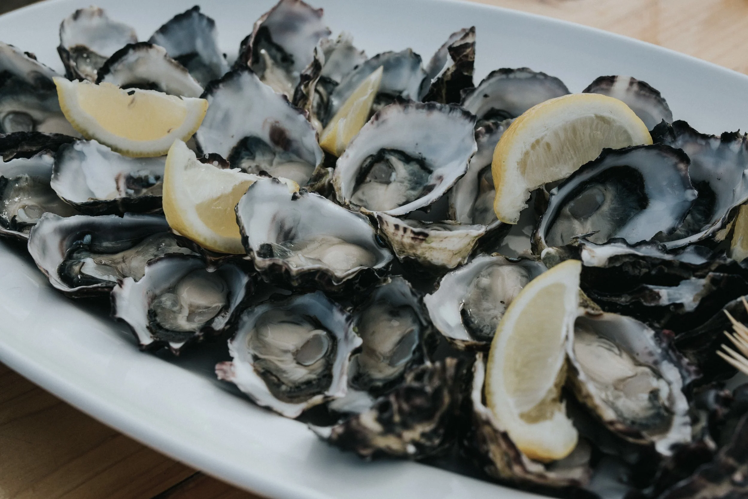 A white platter filled with freshly shucked oysters garnished with lemon wedges.