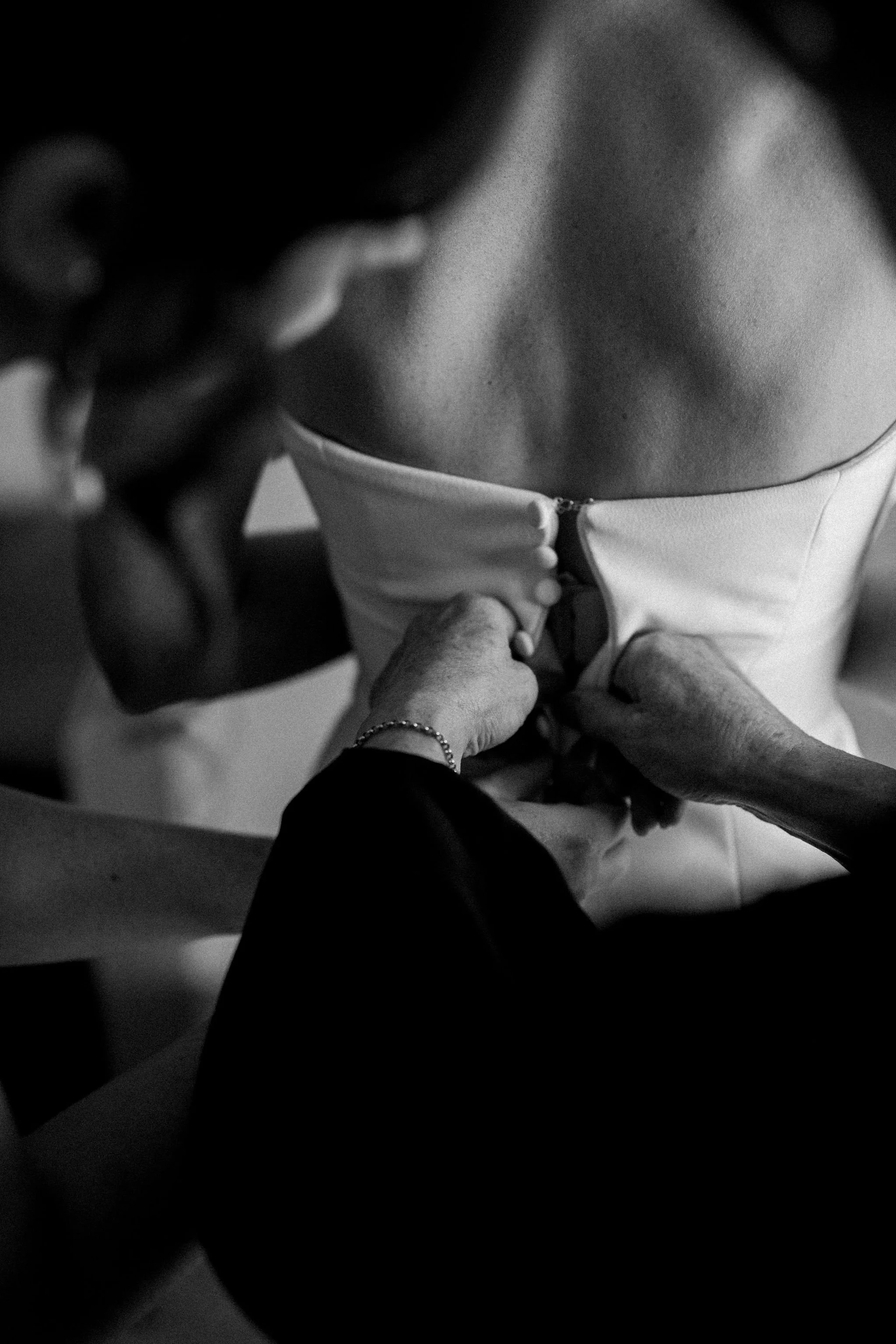 A woman in a strapless dress is having her back zipped up by another person.