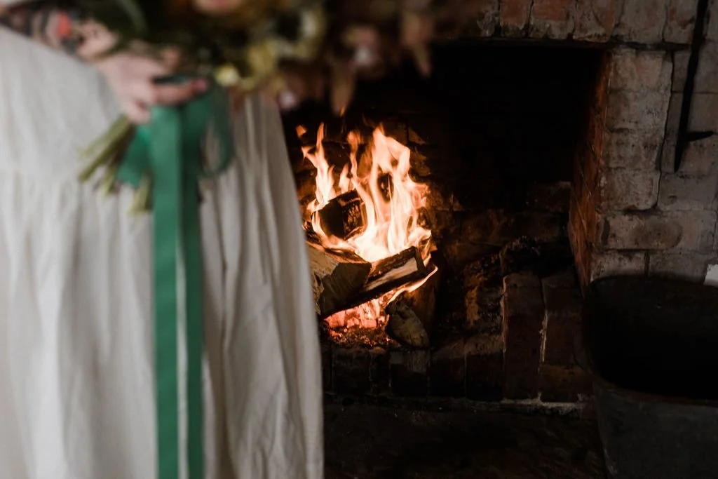 A fireplace with burning logs and flames, partially obscured by a person holding a bouquet of flowers.