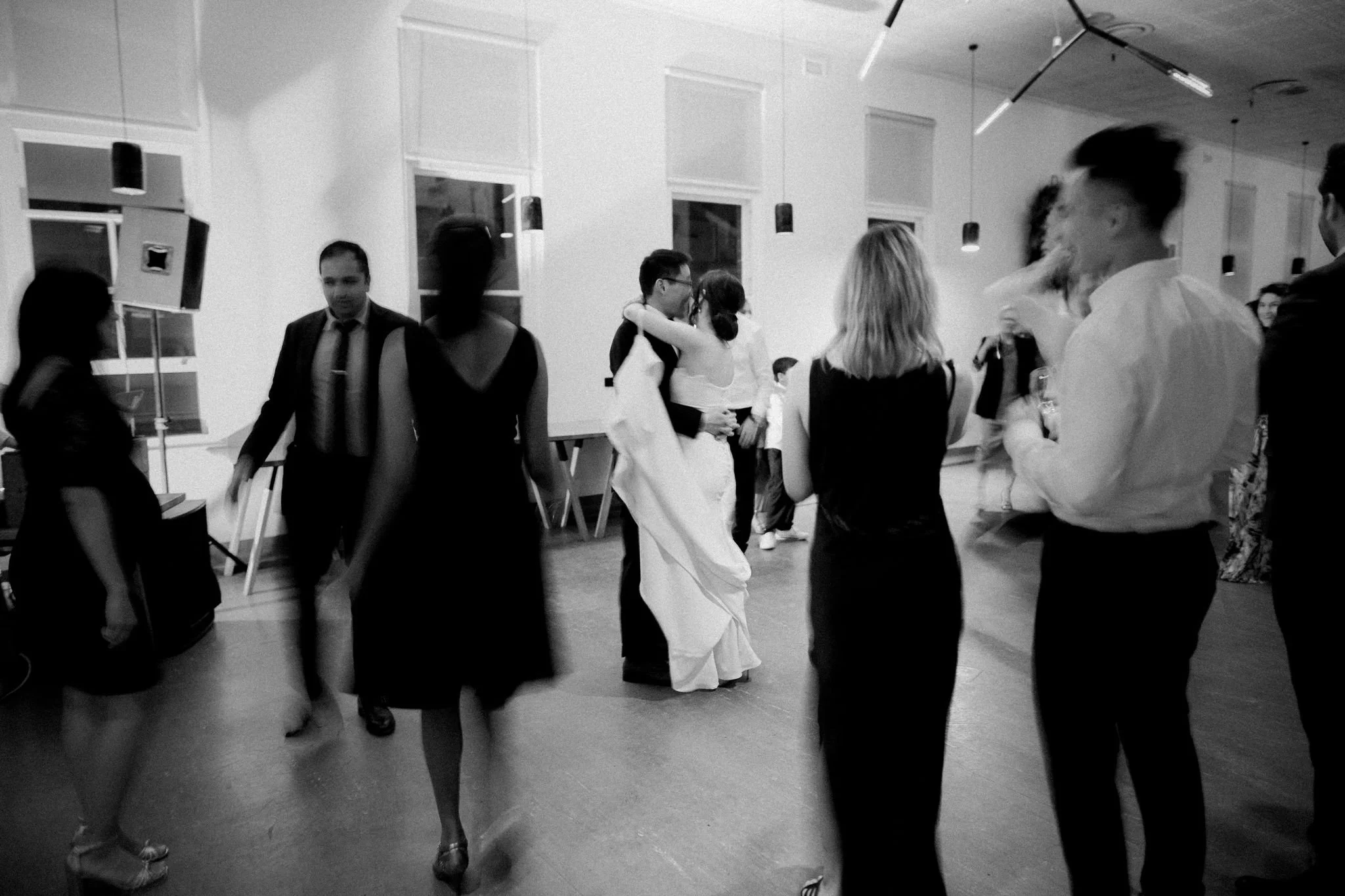 People dancing and socializing at a wedding reception with a bride and groom in the center sharing a dance.