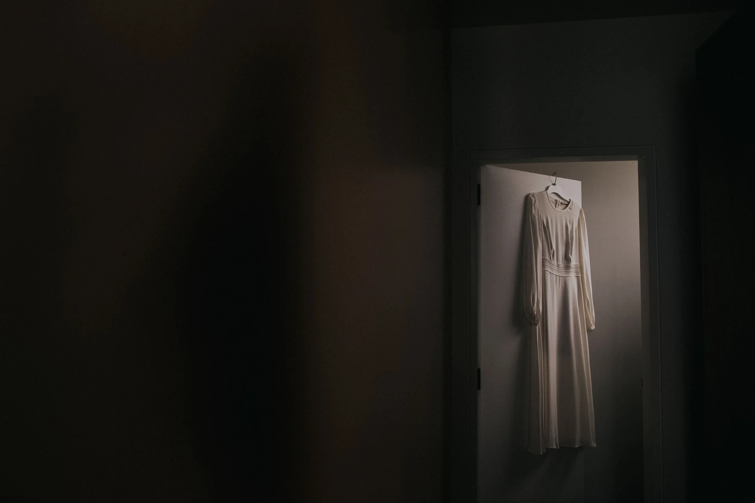 A long white dress hanging on a door in a dimly lit room.