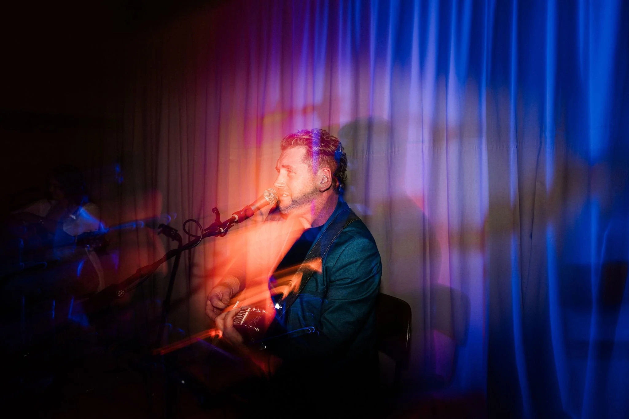 Musician singing into a microphone with colorful light effects and a blurred background.