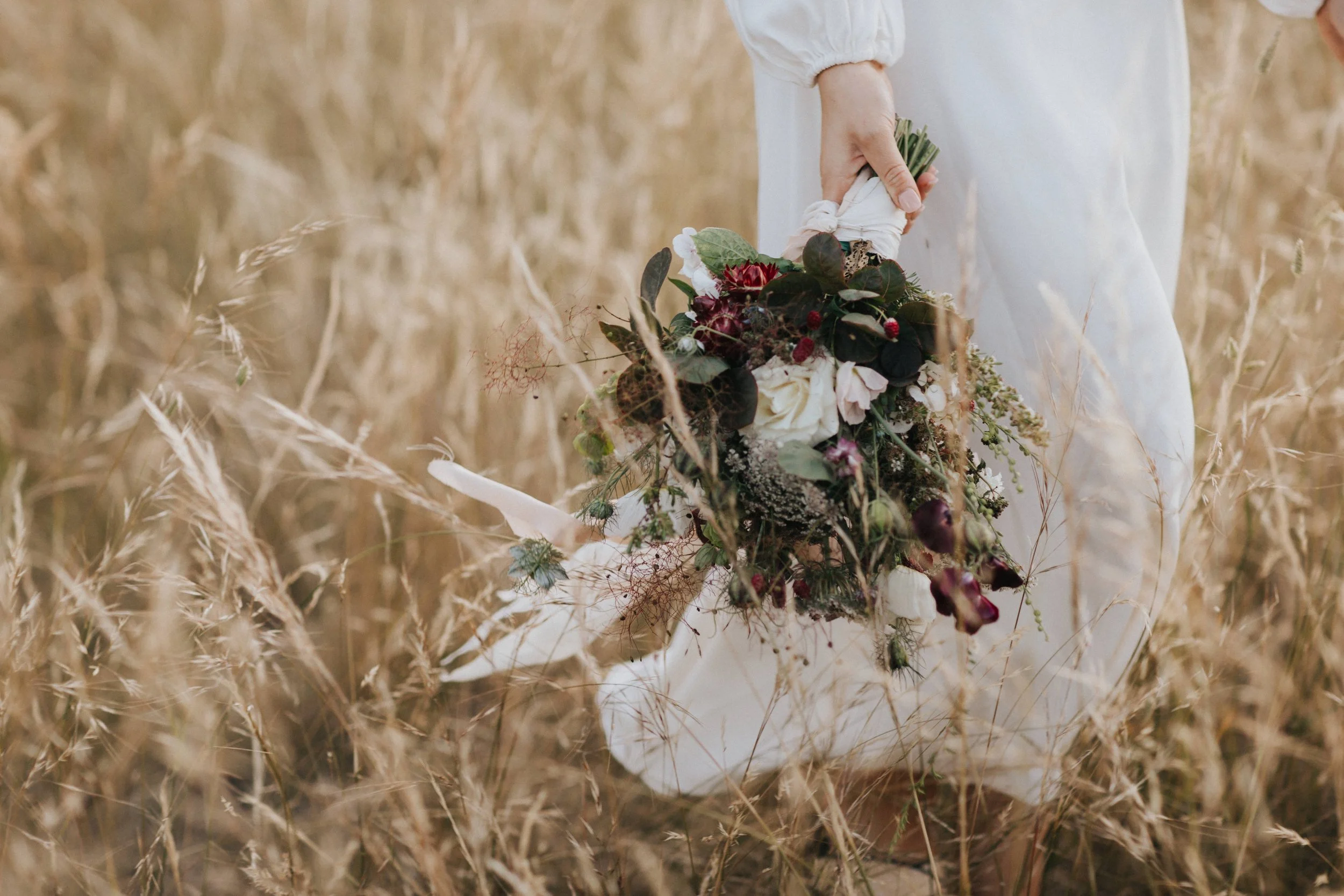 Close-up of a person holding a bouquet of flowers in a field of tall, golden grass.