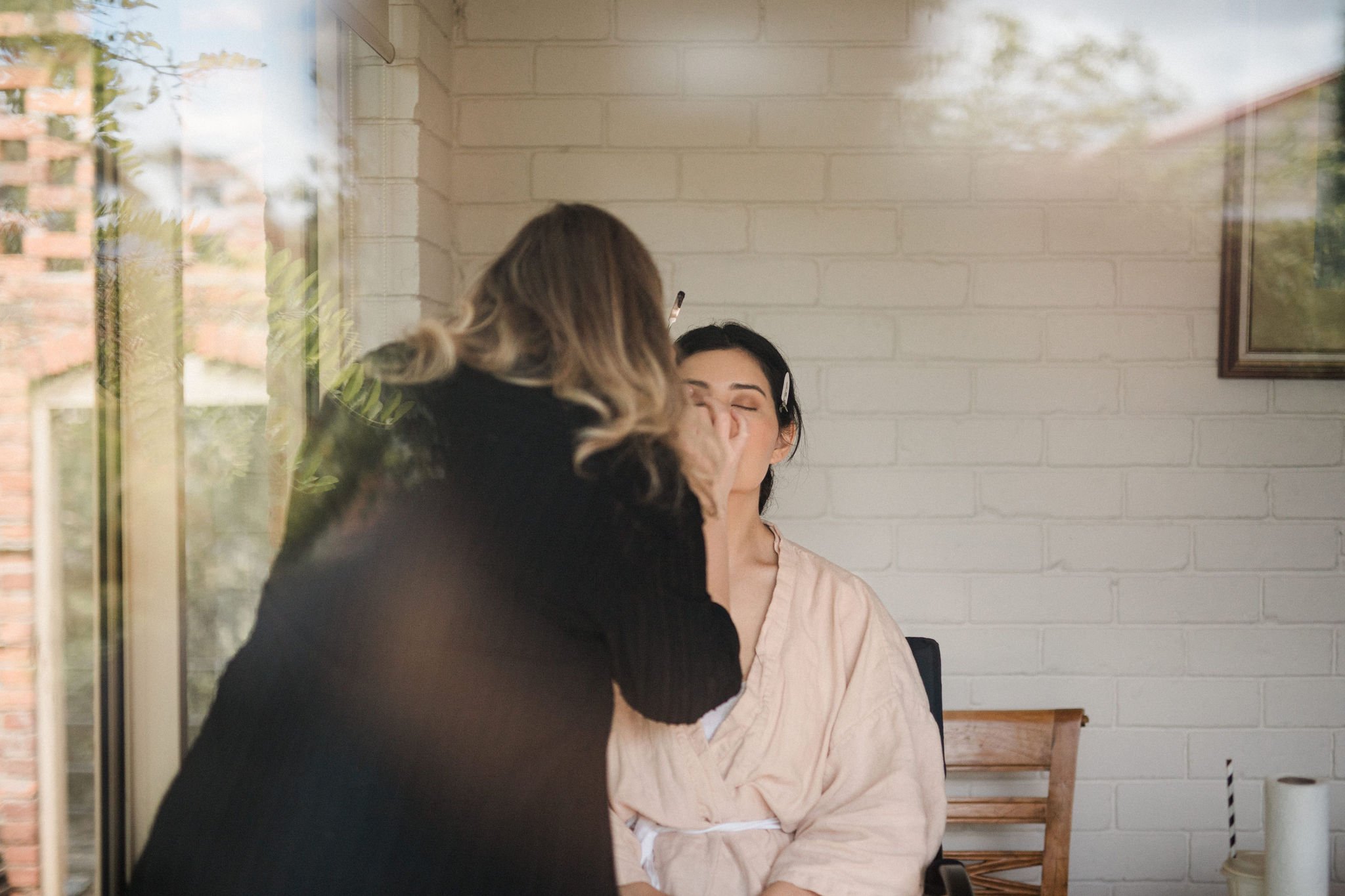 Makeup artist applies eyeshadow to a woman seated in a makeup chair in an indoor room.