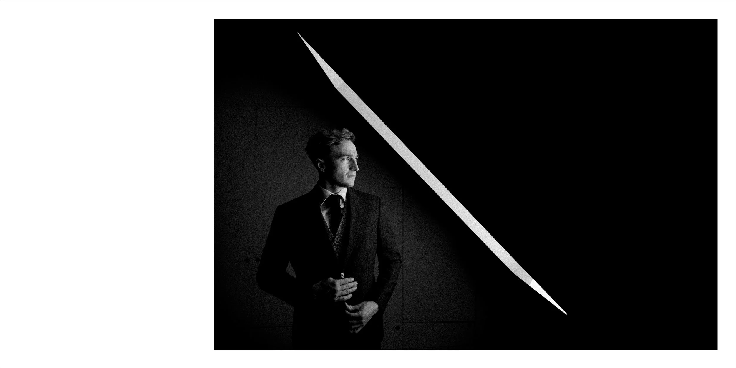 Black and white photo of a man in a suit looking to the left, with a diagonal light beam shining across the top right corner.