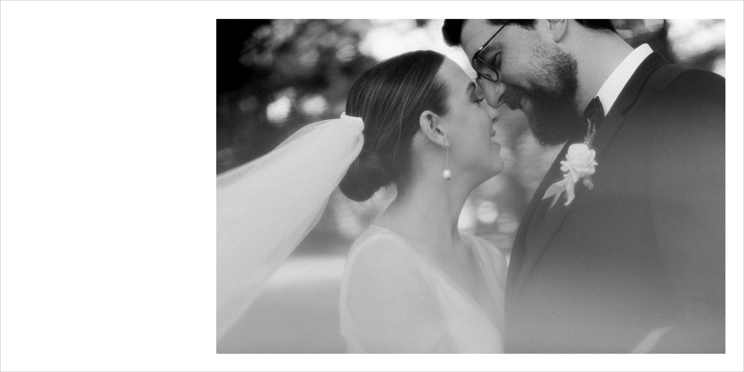 Black and white photo of a bride and groom touching foreheads outdoors, with blurred trees in the background, capturing an intimate moment on their wedding day.