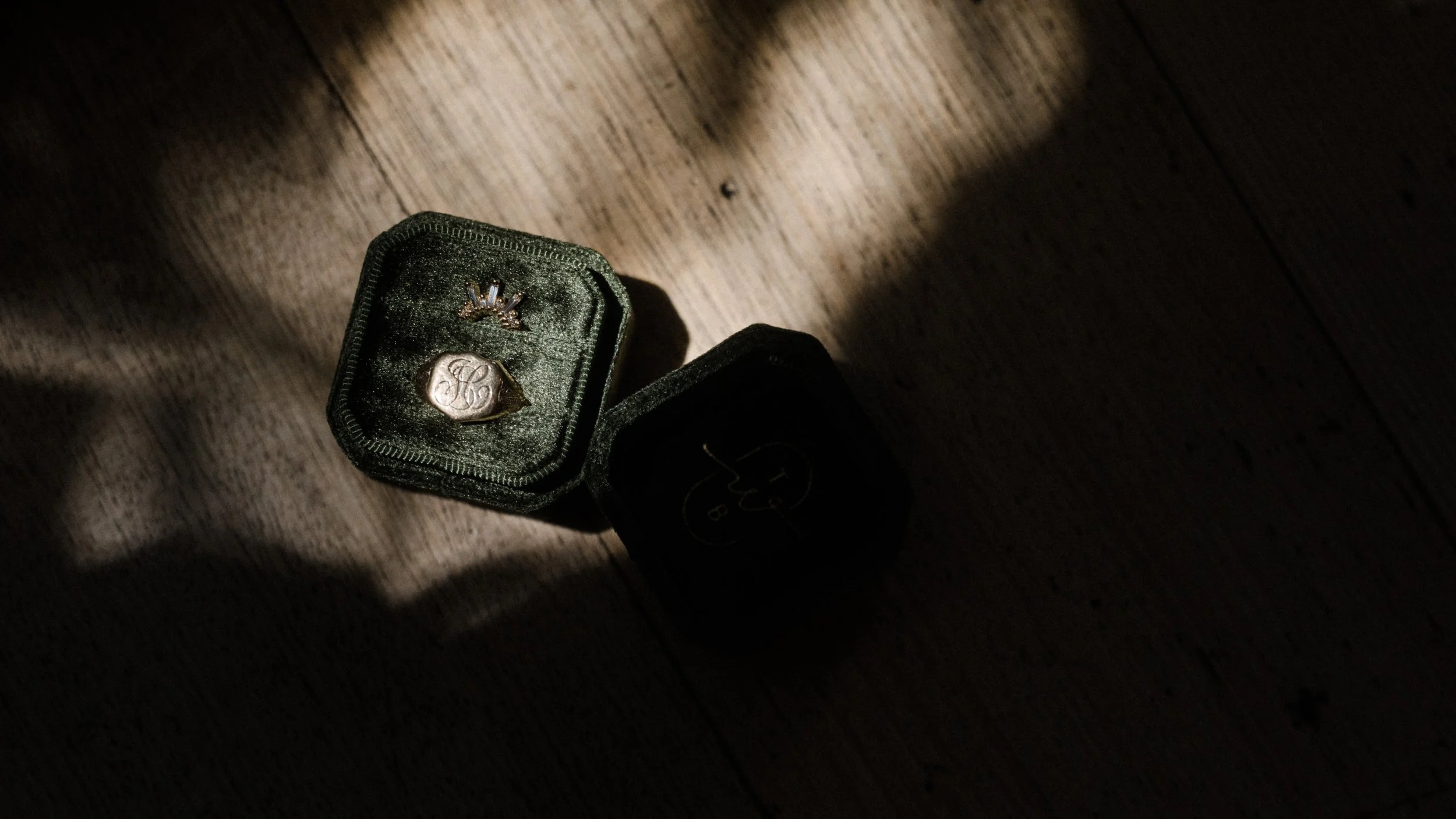A small green velvet jewelry box containing rings, placed on a wooden surface in shadow and light.