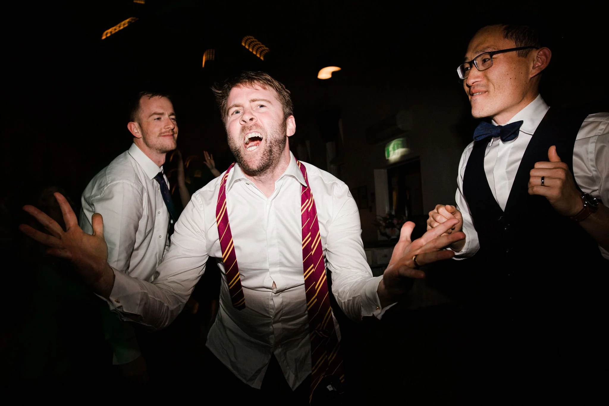 Men dancing at a party, dressed in formal attire with shirts and ties, in a dark indoor setting