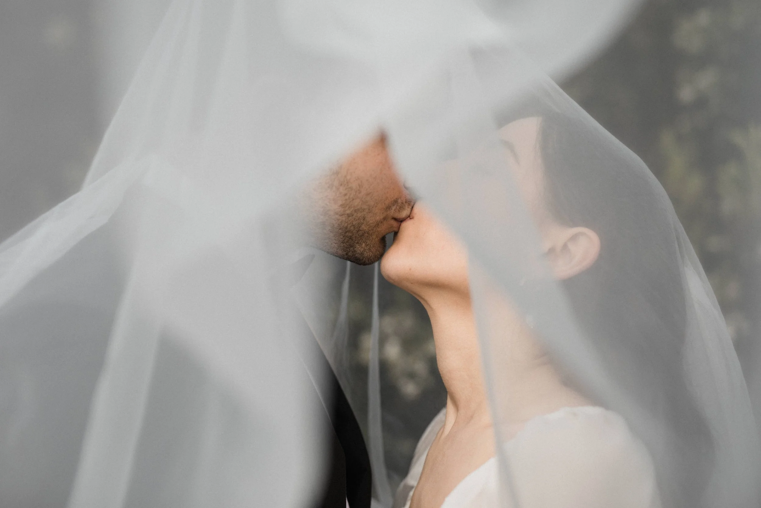 A close-up of a bride and groom kissing under a wedding veil.