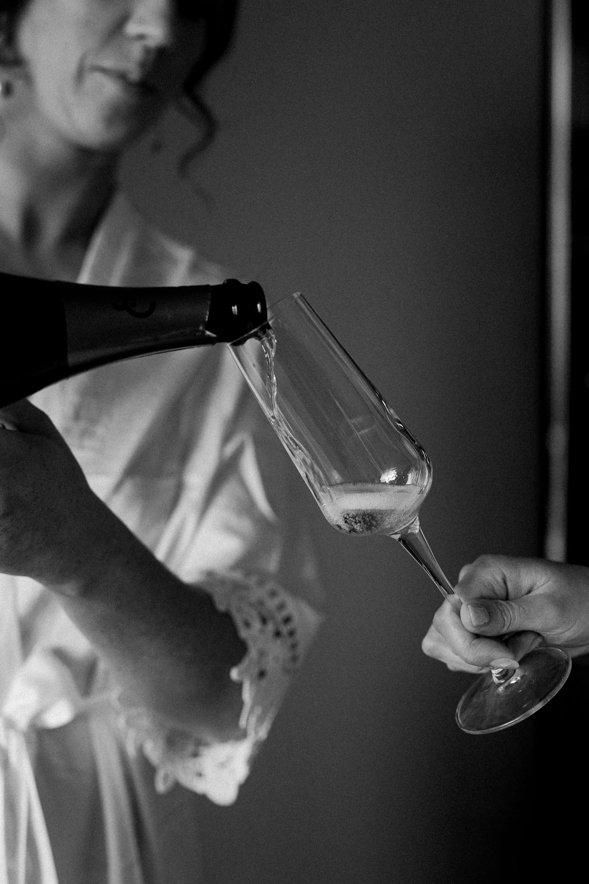 A woman in a light-colored dress is pouring champagne into a glass held by another person.