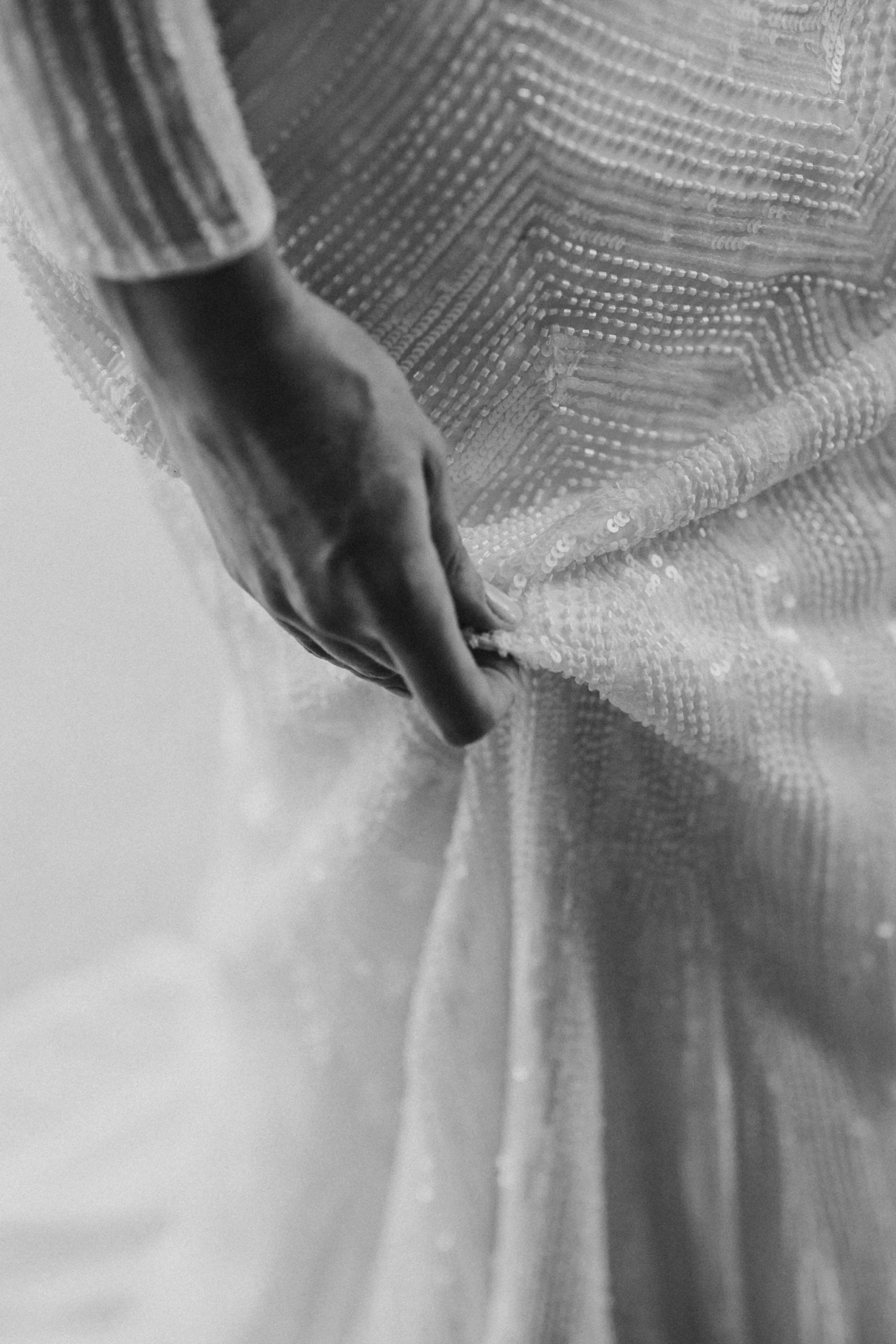 Close-up of a person's hand holding a fabric with sequins, in black and white.