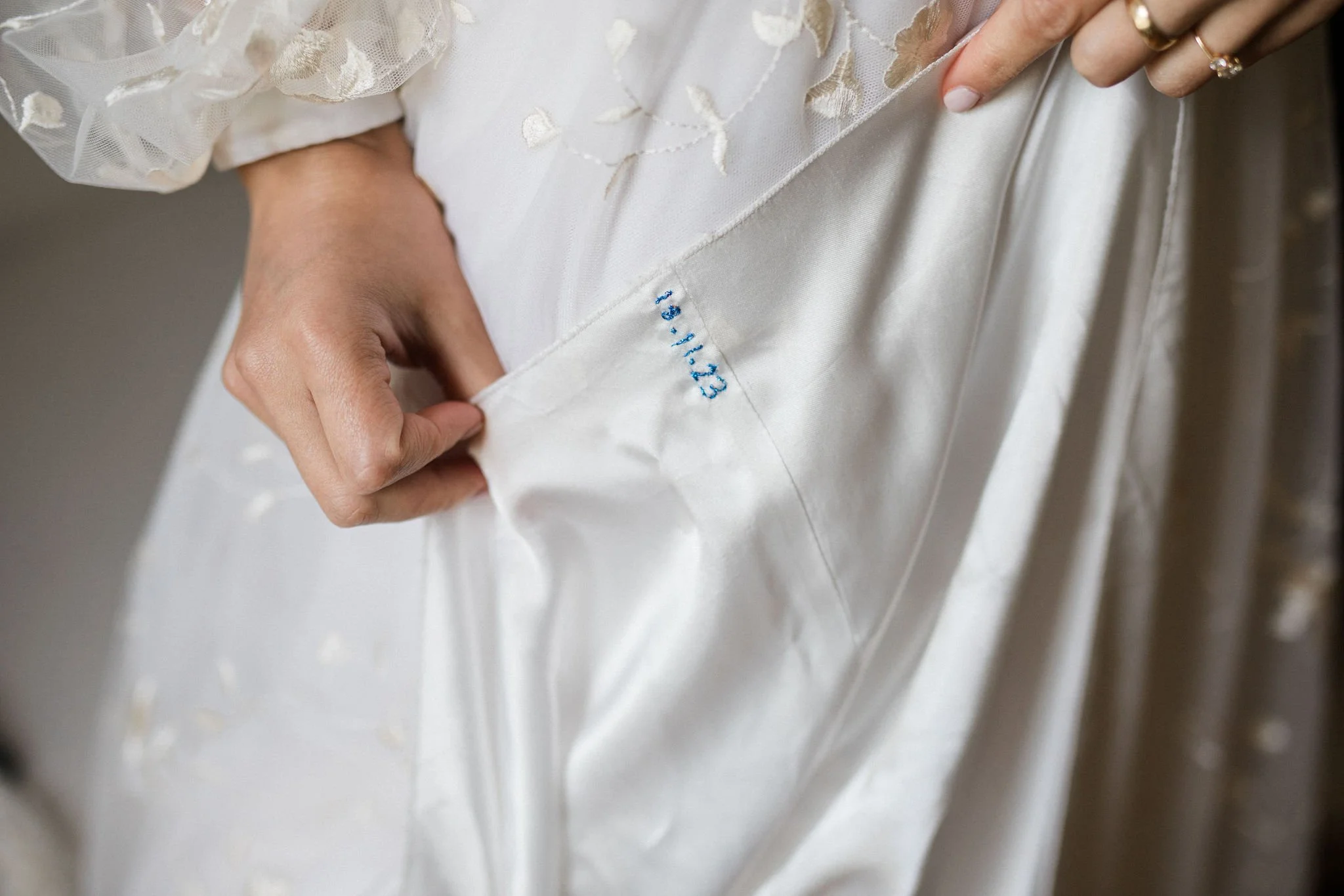 Close-up of a person holding the hem of a white wedding dress, showing blue embroidery.