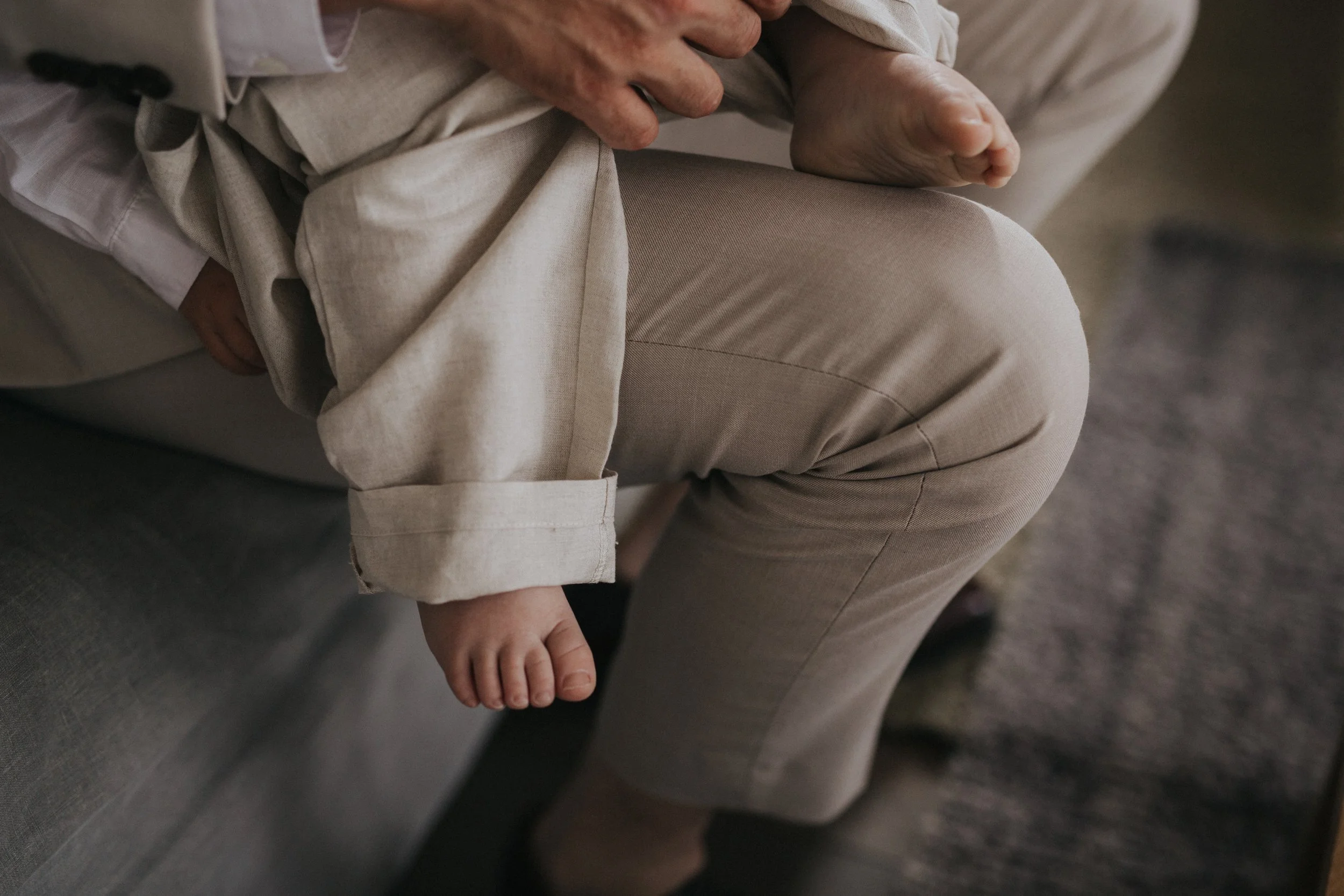 Close-up of a father's lap with a child sitting on their lap, showing the child's tiny foot hanging down.