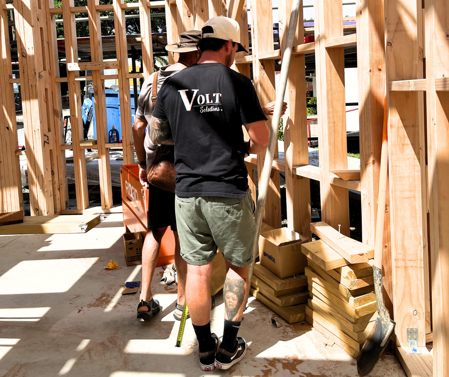 Two people working on framing a wooden structure at a construction site, with tools and wood around them.